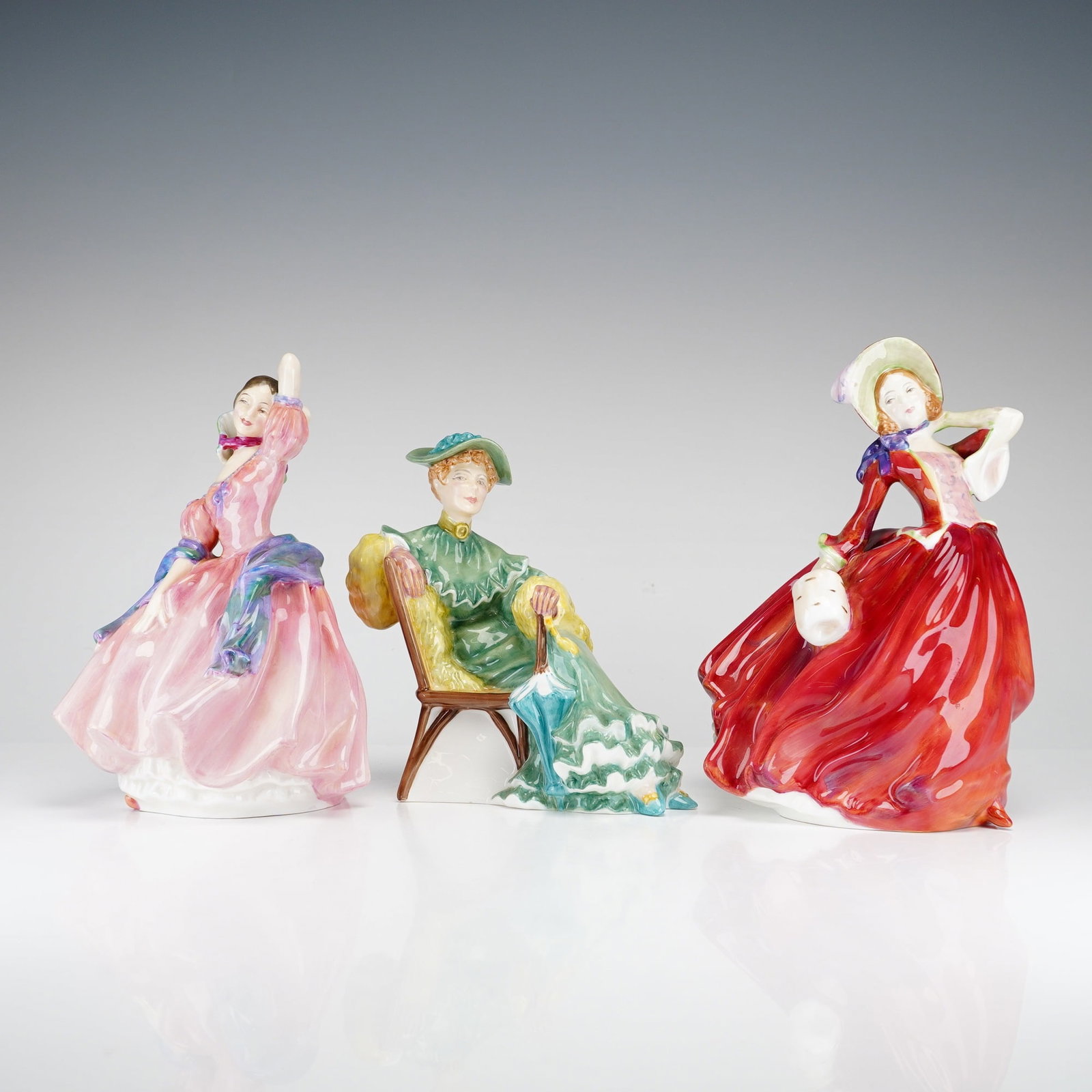 3pc Royal Doulton Figurines Maytime, Ascot, and Autumn Breezes: This lot consists of three hand-painted glazed porcelain figurines by Royal Doulton, England, depicting elegantly dressed female figures. The collection includes Maytime (HN 2113), modeled as a standi