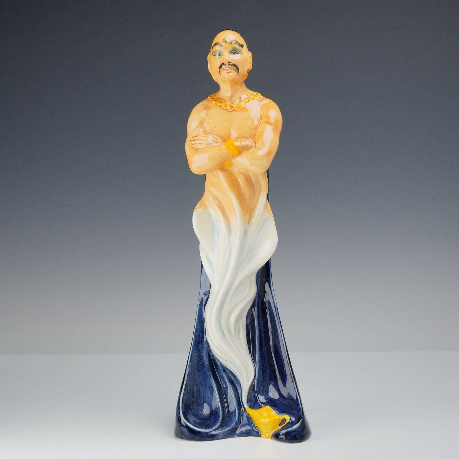 Royal Doulton Porcelain Figurine The Genie HN 2989: This Royal Doulton glazed porcelain figurine, titled The Genie and identified as model HN 2989, features a bald male figure with a black topknot, green eye makeup, and a mustache. The figure is depict