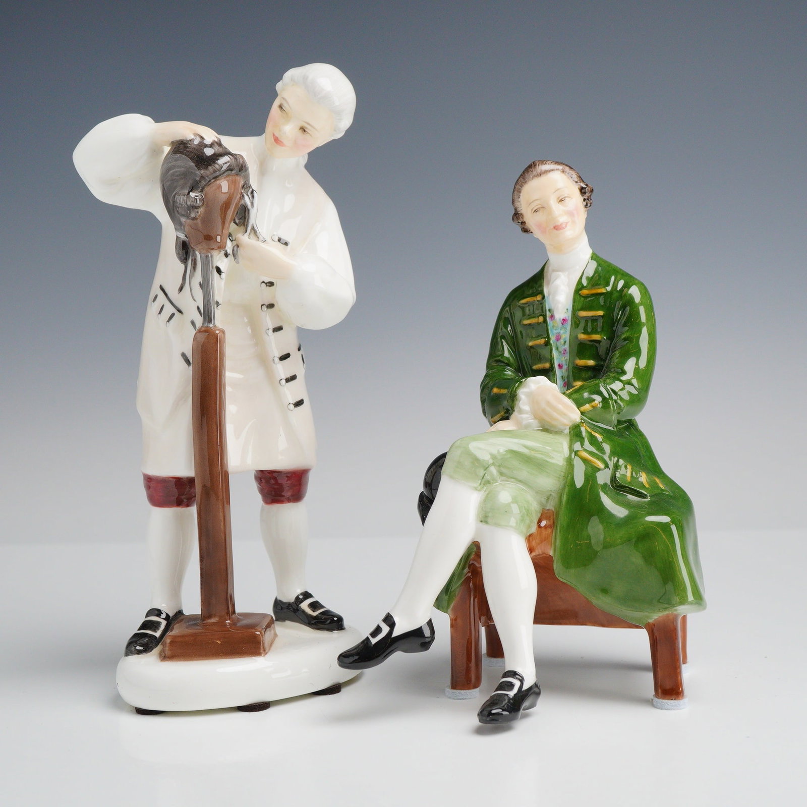 Two Royal Doulton Porcelain Figurines, The Wigmaker of Williamsburg HN 2239 and A Gentleman from: A group of Royal Doulton hand-painted polychrome glazed porcelain figurines from the Colonial Williamsburg series. The first figurine, titled The Wigmaker of Williamsburg (model HN 2239), depicts a st