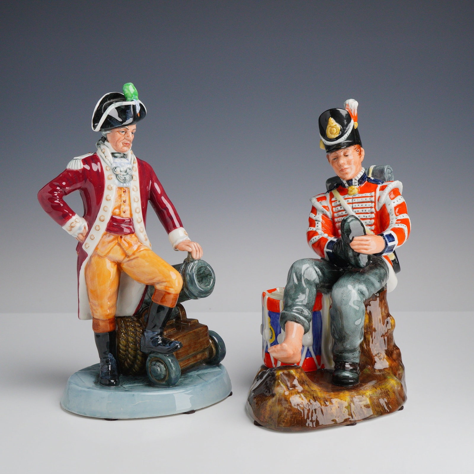 2pc Royal Doulton Porcelain Figurines Officer of the Line HN 2733 and Drummer Boy HN 2679: This lot consists of two Royal Doulton hand-painted glazed porcelain figurines depicting British military subjects. The first figurine, titled Officer of the Line (HN 2733), depicts an 18th-century of
