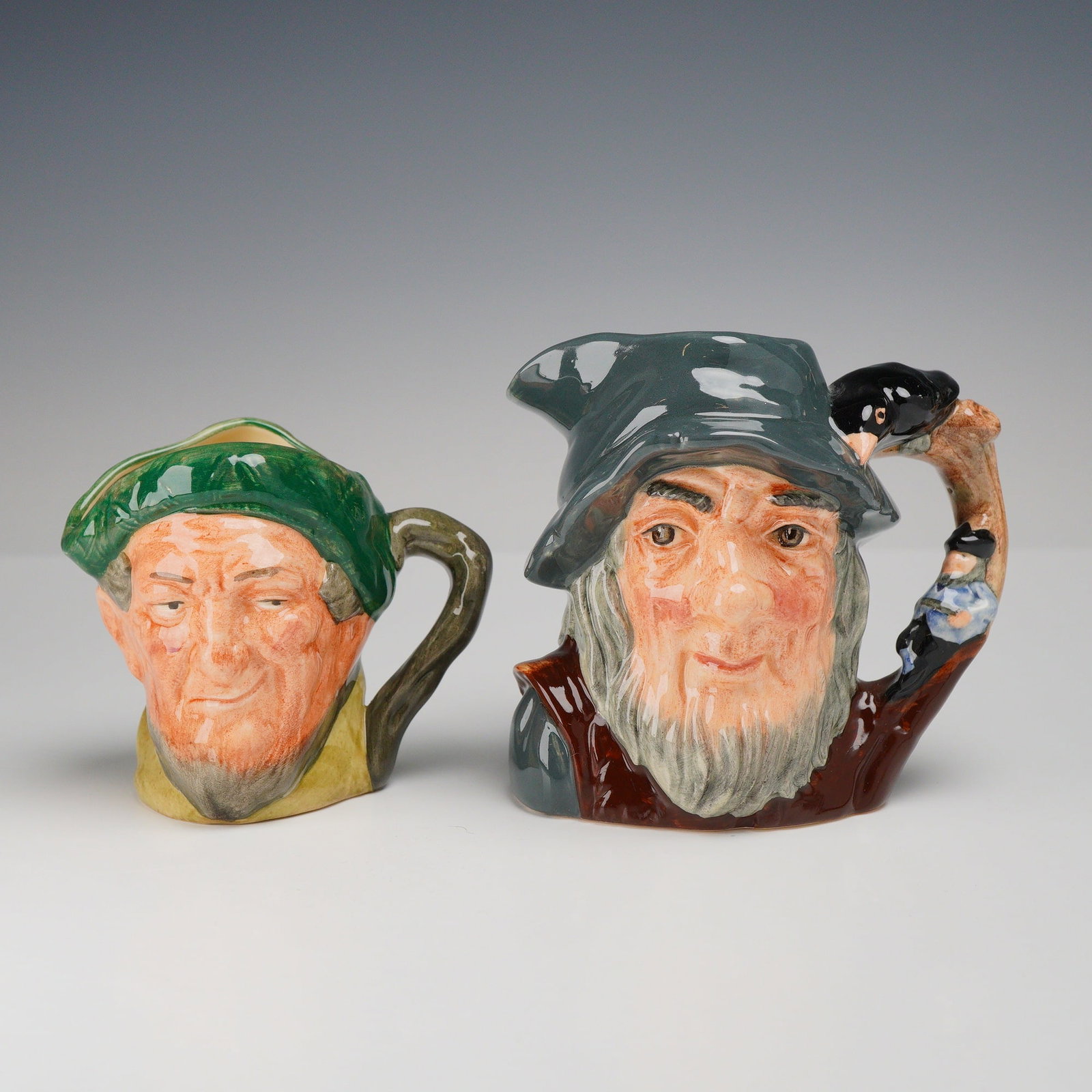 2pc Royal Doulton Character Jugs, Rip Van Winkle D6463 and Auld Mac D5824: This lot consists of two glazed ceramic character jugs manufactured by Royal Doulton. The larger jug depicts the literary figure Rip Van Winkle, featuring a long gray beard and a wide-brimmed gray hat