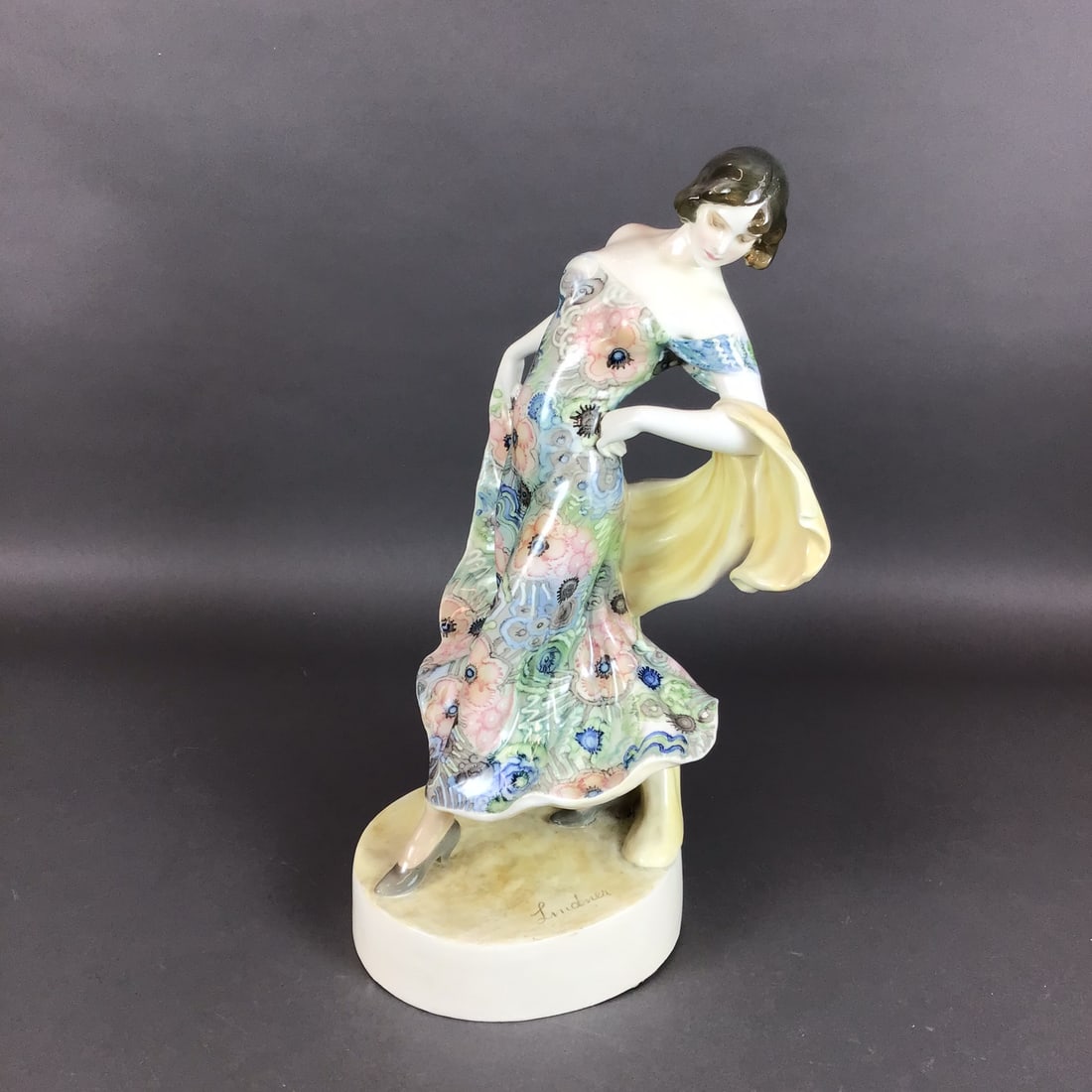 Goldscheider Wien Large Porcelain Figure Dancer in Spinning Movement Signed Lindner: This large porcelain figure, produced by the Goldscheider manufactory in Vienna, Austria, depicts a woman in a dynamic posing stance. The subject is dressed in a form-fitting, off-the-shoulder gown de