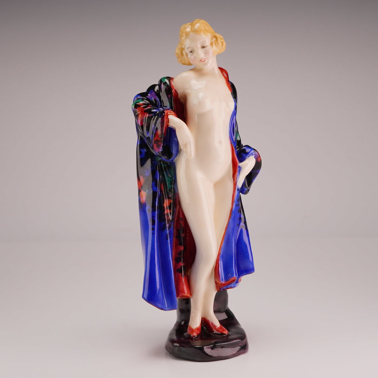 Royal Doulton by Leslie Harradine Figurine, The Bather HN774, Rare Version: The Art Deco style figure depicts a standing female nude with blonde hair and red heels, partially draped in a patterned robe featuring a color palette of cobalt blue, red, green, and black. The figur
