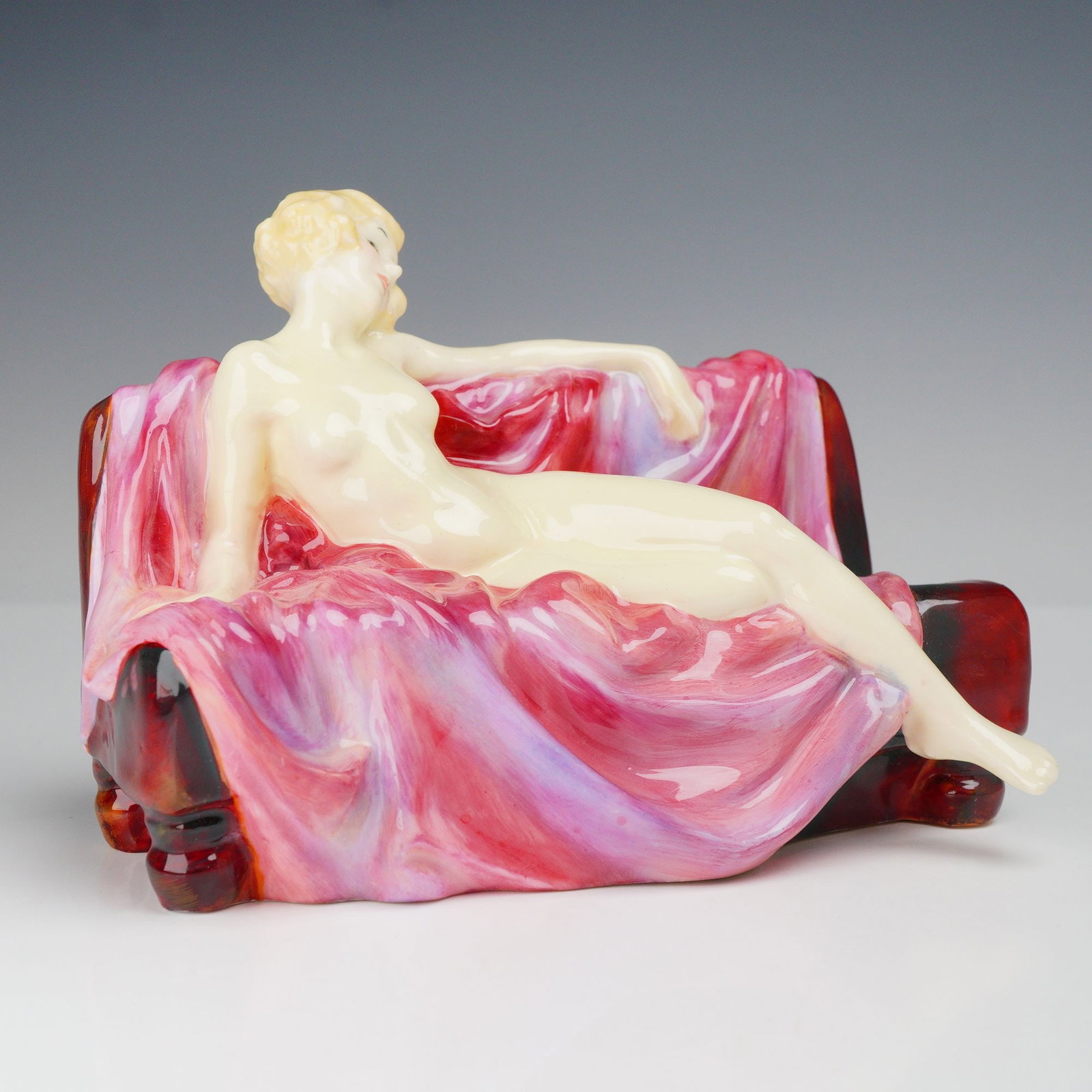 Royal Doulton Art Deco Porcelain Figurine Siesta HN 1305: This glazed porcelain figurine, titled Siesta, was produced by Royal Doulton and designed by Leslie Harradine. The model depicts a reclining nude female figure with blonde hair styled in finger waves 