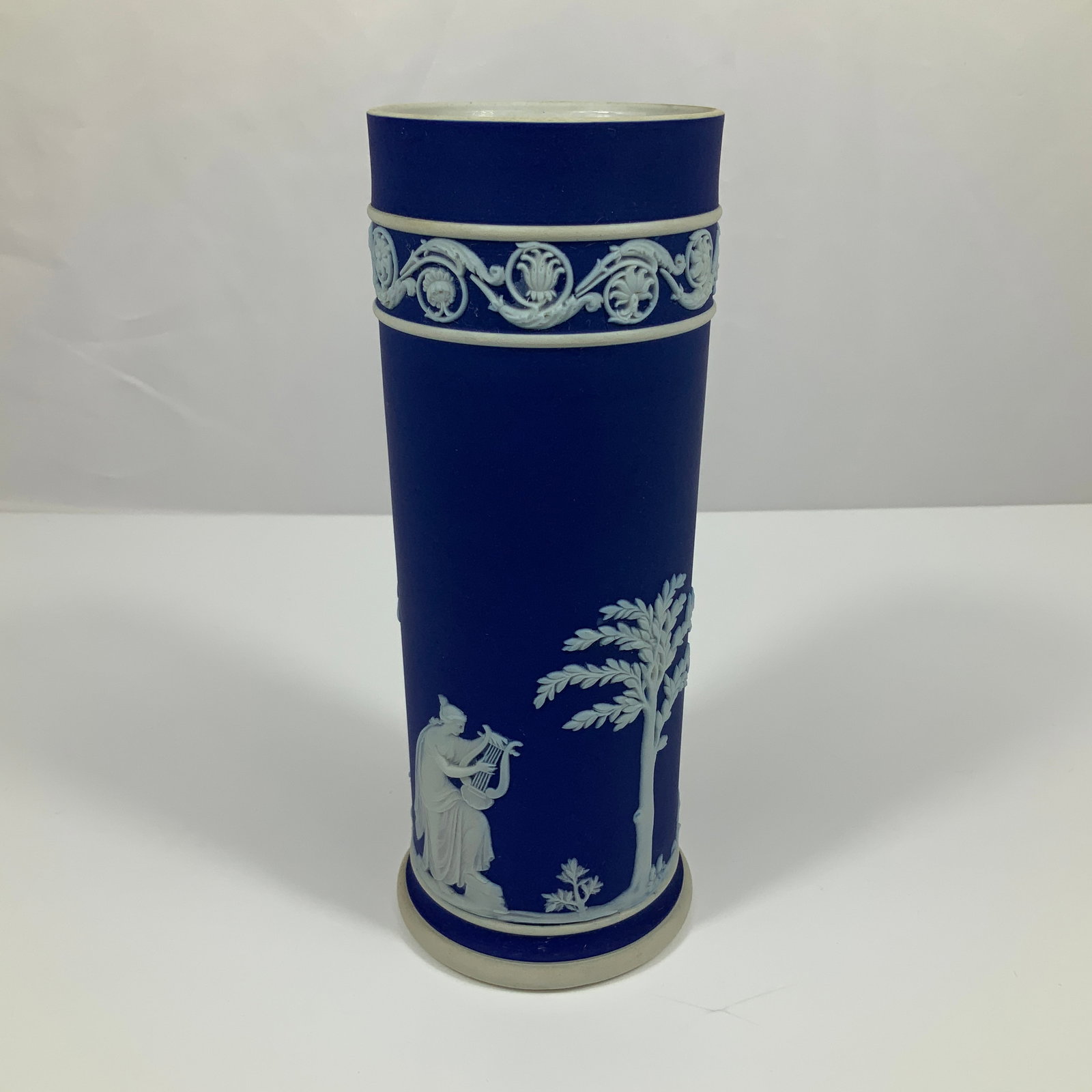 Wedgwood Cobalt Blue Jasperware Cylindrical Spill Vase: This cylindrical spill vase is manufactured by Wedgwood in cobalt blue Jasperware stoneware. The exterior features applied white bas-relief sprigged decoration in a neoclassical style. The main body d