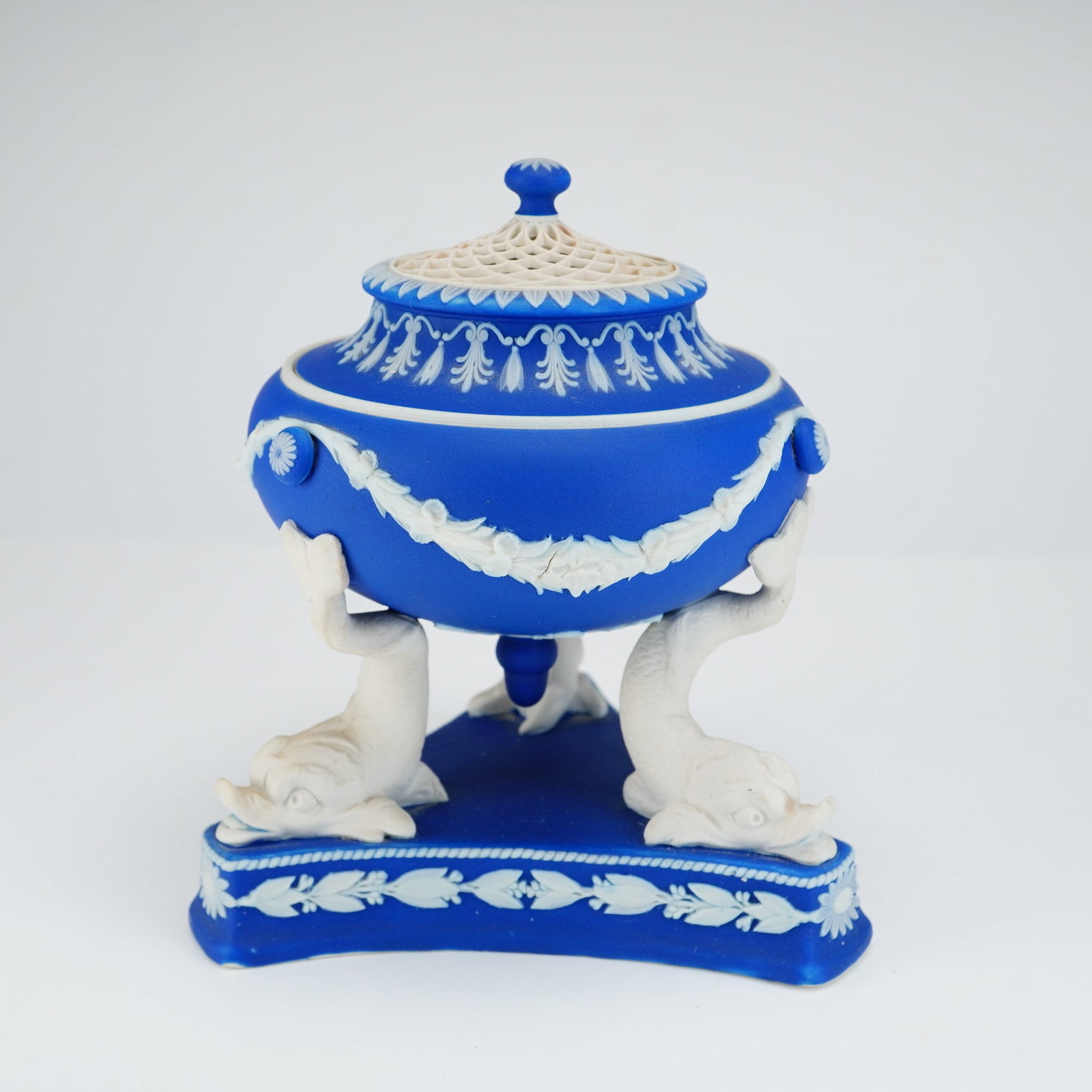Wedgwood Dark Blue Jasperware Dolphin Pastille Burner and Cover: A Wedgwood jasperware pastille burner and cover featuring a dark blue ground with white relief decoration. The vessel is designed with an urn-form bowl supported by three white jasper dolphins that re