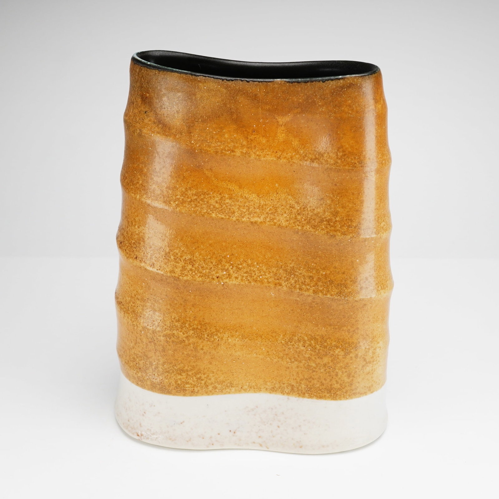 Mark Shapiro Studio Pottery Ribbed Stoneware Vessel: The tall, hand-built piece is of oval section and features prominent undulating horizontal ribbed bands. Glazed surface transitions into a cream-white slip or clay body at the base. The interior is