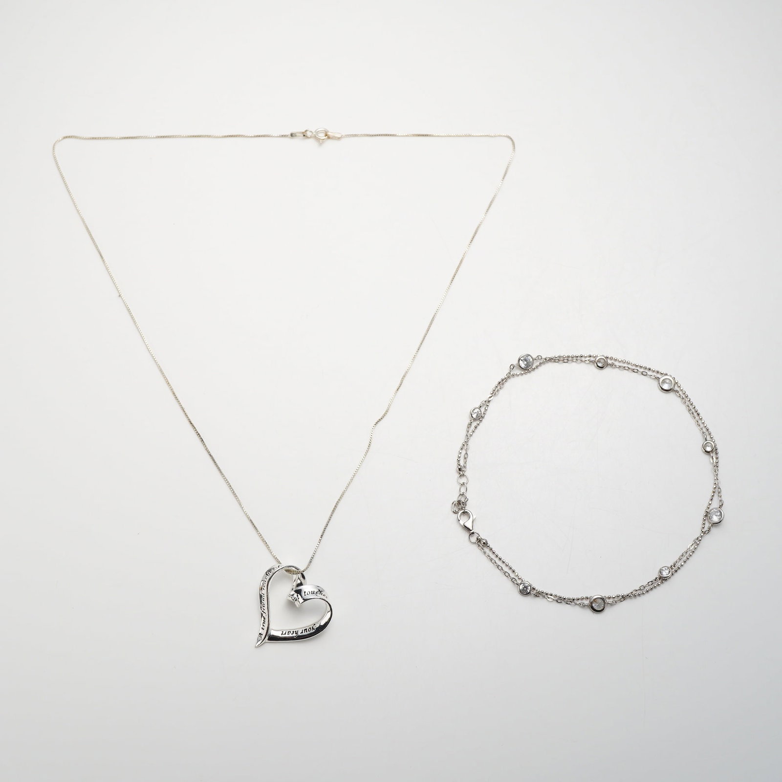 2pc Sterling Silver Heart Pendant Necklace and Double-Strand Bracelet Jewelry: This two-piece sterling silver set includes a pendant necklace and a double-strand bracelet. The necklace features an open heart pendant with an intertwined ribbon inscribed: "A true friend reaches fo