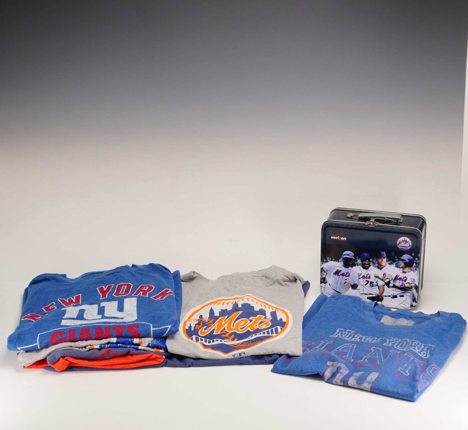 8pc New York Sports Grouping in Large and Extra Large Sizes with New York Mets Verizon Promotional: This lot consists of an 8pc grouping of New York professional sports apparel and memorabilia representing the New York Giants NFL and New York Mets MLB teams. The collection includes various shirts an