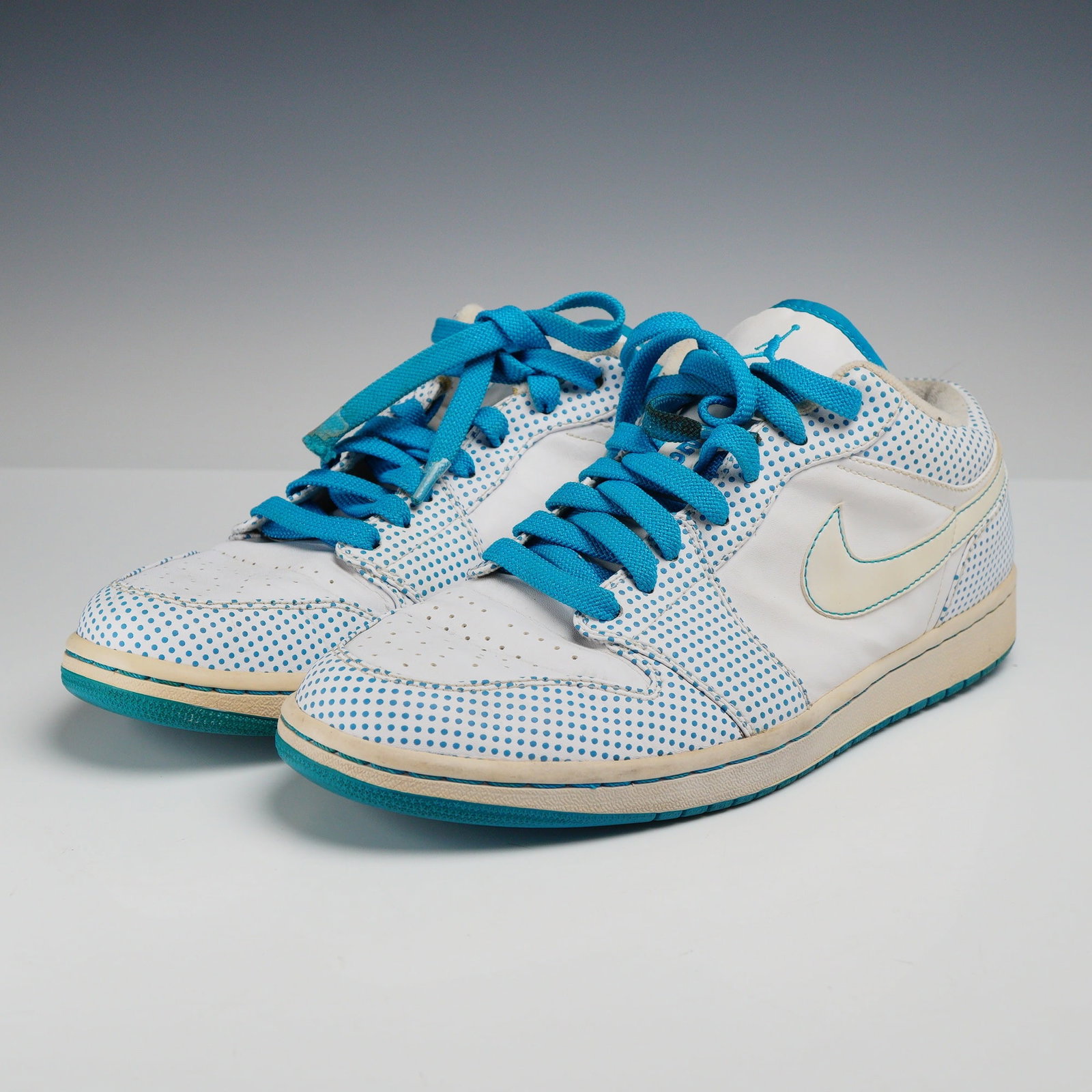 A Pair of Men's Nike Air Jordan 1 Phat Low Laser Blue Sneakers, Size 12: This pair of men's Nike Air Jordan 1 Phat Low sneakers is identified as the Laser Blue colorway. The sneakers feature a low-top silhouette with a white leather upper base. Overlays on the toe, eyestay