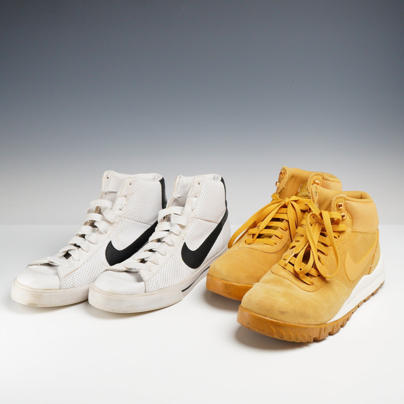 Two Pairs of Nike Men's Sneakers Including Blazer High and Manoa, Size US 12: This lot consists of two pairs of men's Nike high-top sneakers, both size US 12. The first pair is the Nike Blazer High, style code 354701-101. It is constructed with a white perforated leather upper,