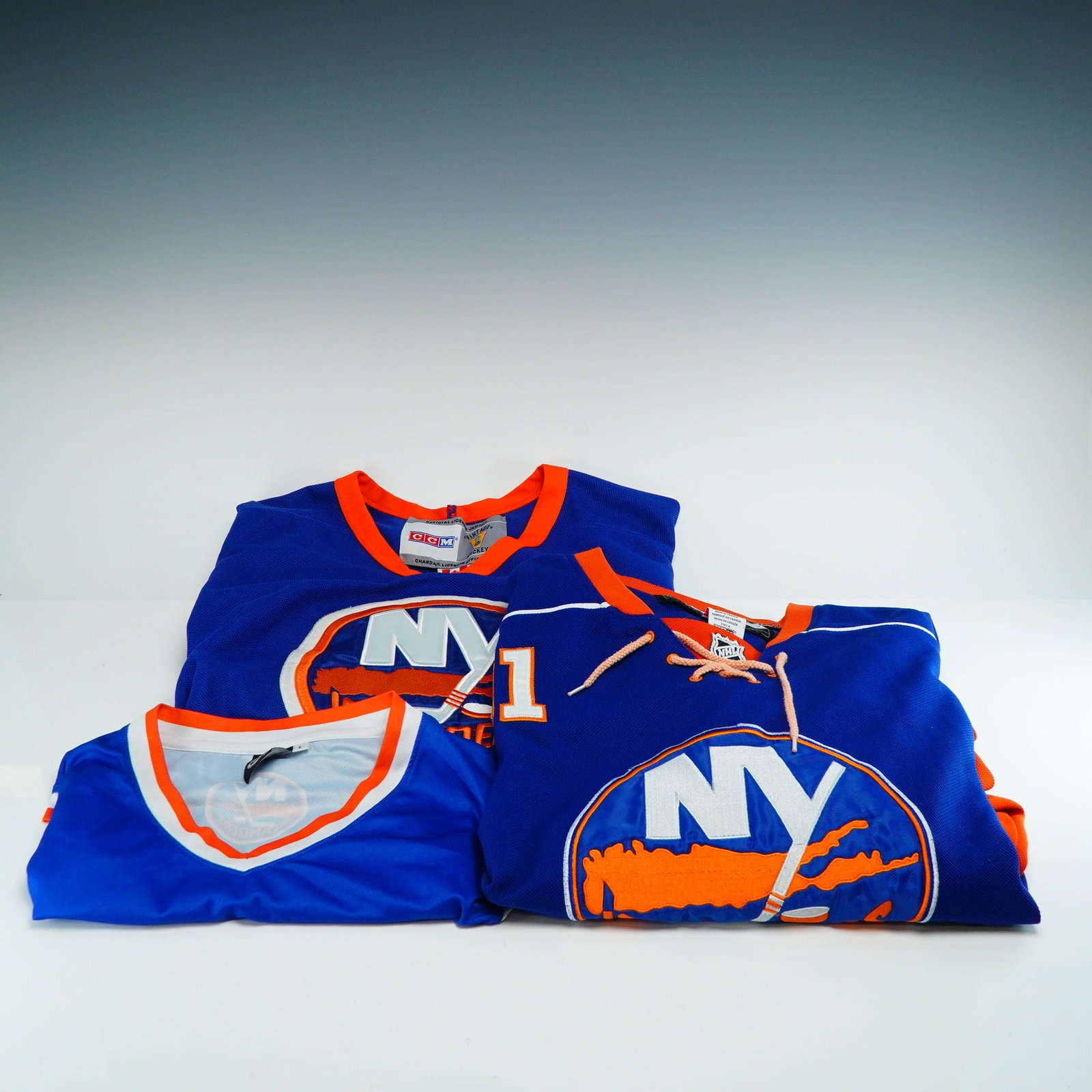 3pc New York Islanders Hockey Jerseys: A collection of three New York Islanders NHL hockey jerseys offered as-is. This lot includes one professional-grade authentic jersey, one licensed vintage reproduction, and one licensed fan replica. T