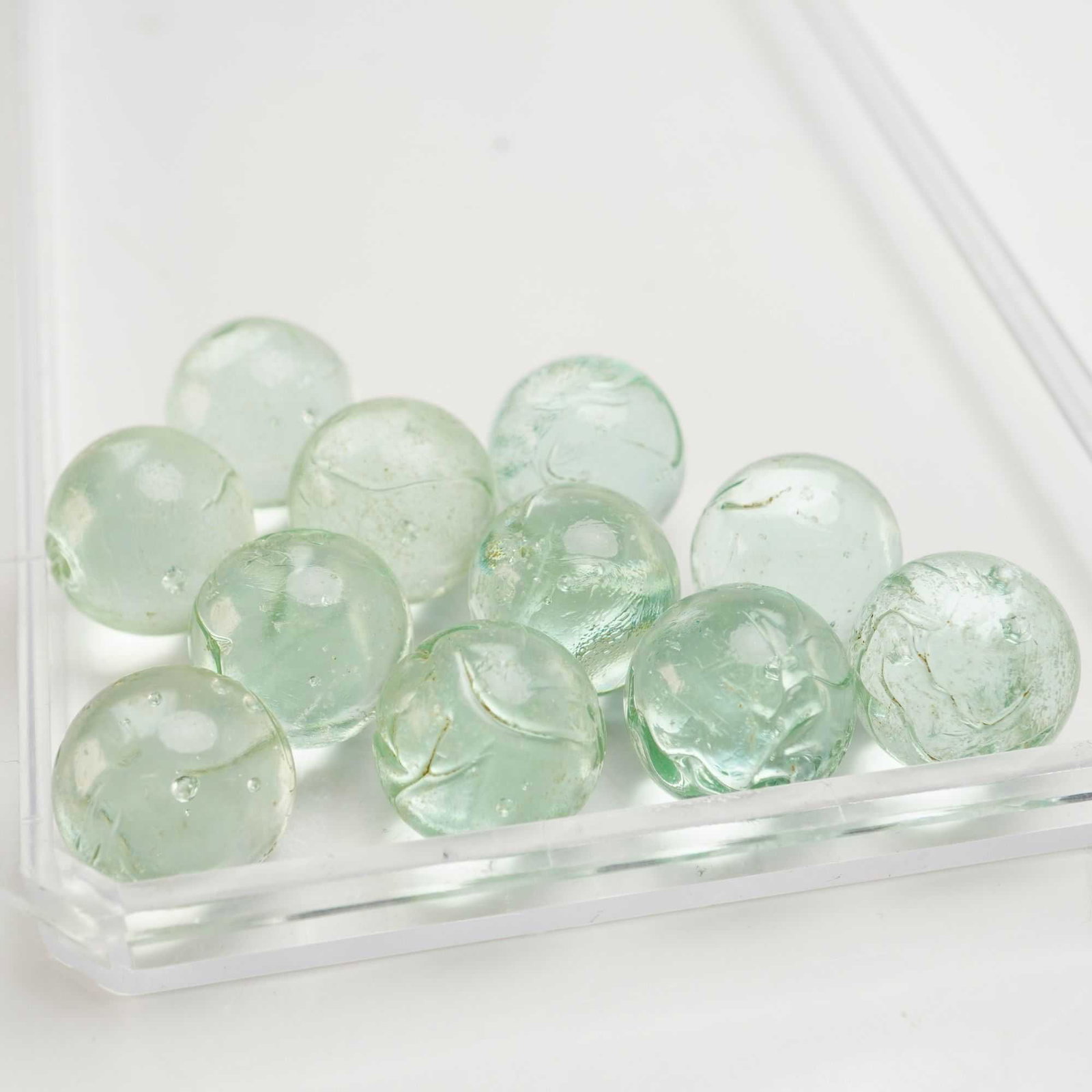 11pc Clear Glass Shooter Marbles: A collection of eleven glass shooter marbles with an unpolished surface and a light green tint. Dimensions: 20.6 mm in diameter Weight: 4.7 oz