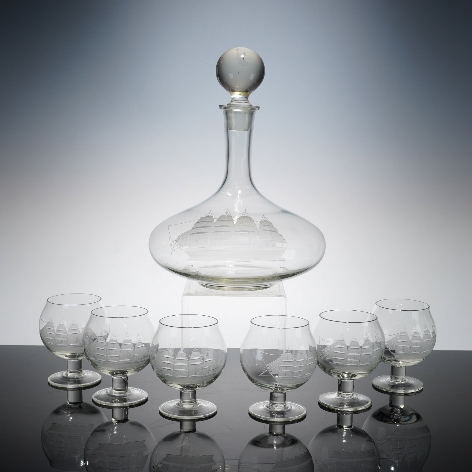7pc Brandy Glasses with Captain's Clipper Ship Decanter: Collection comprising six brandy glasses and one captain's decanter with stopper. Each piece is crafted in clear glass and decorated with a frosted, etched clipper ship motif. The dimensions are