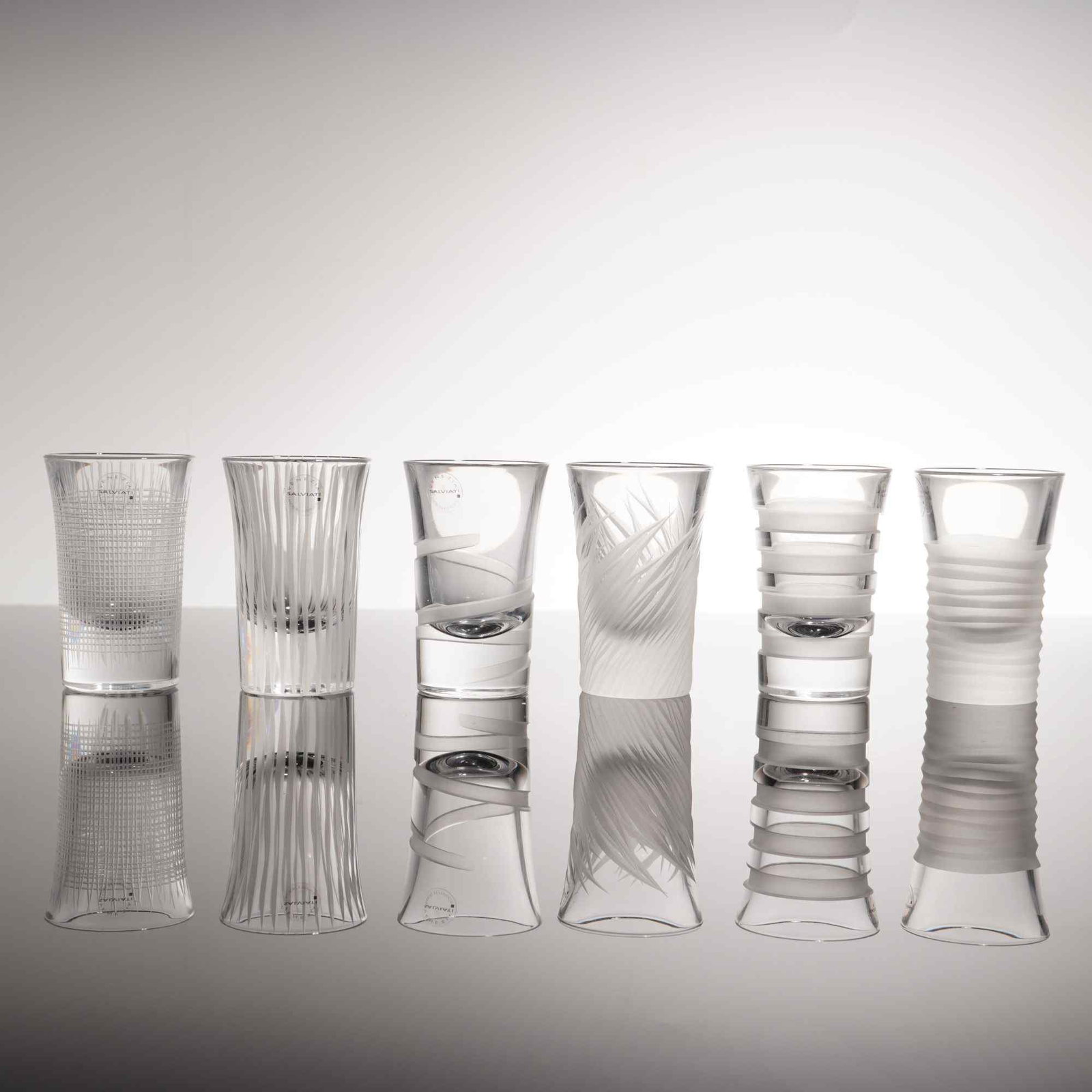 A Set of 6 Salviati Italian Crystal Shot Glasses: This set of six Italian crystal shot glasses is produced by Salviati in Murano, Venice. Each glass is crafted from clear blown glass and features a unique acid-etched frosted pattern. The decorative m