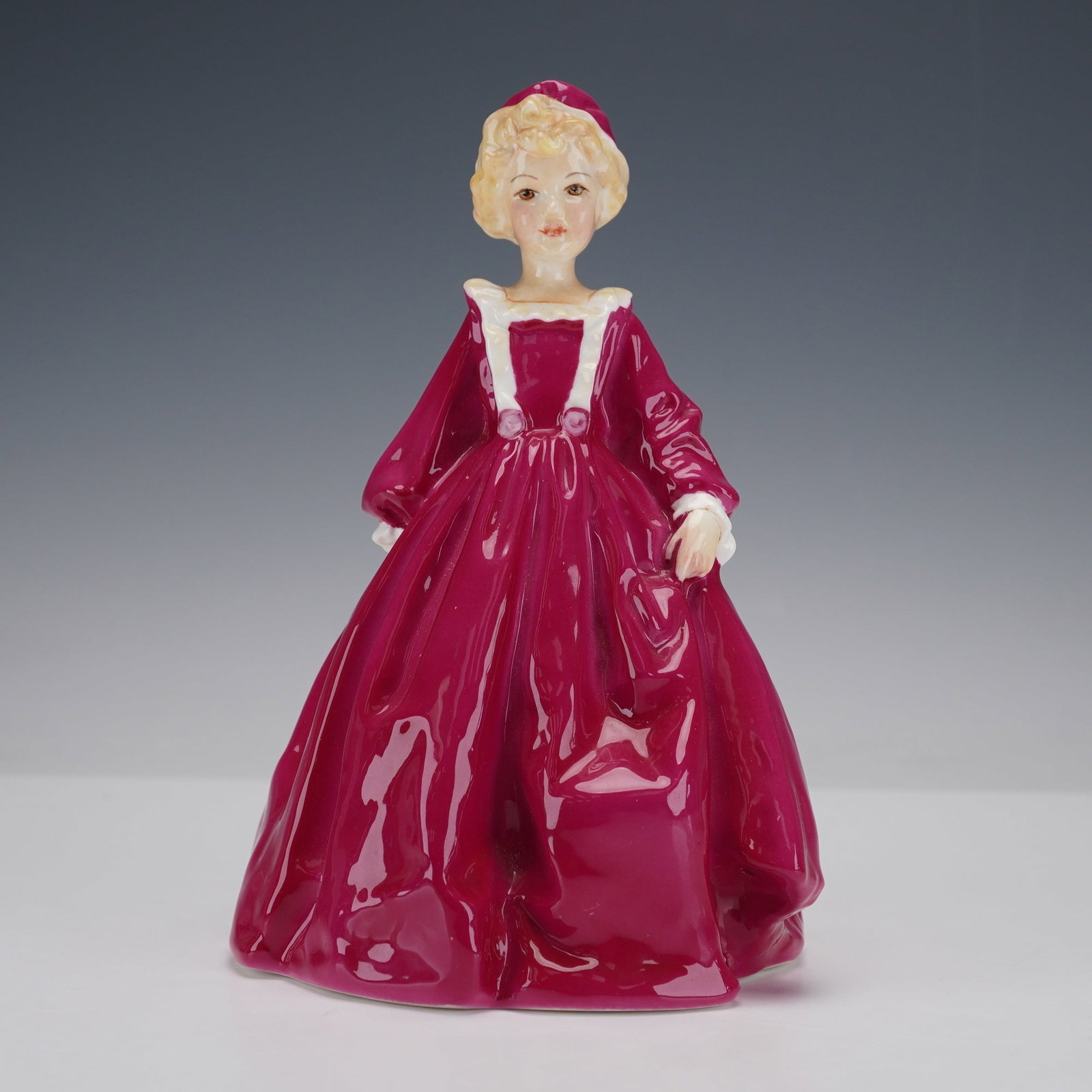 Royal Worcester Figurine, Grandmother's Dress: A charming young girl dressed in her grandmothers elegant gown, finished in a deep rose hue with soft white accents. Her poised stance and gentle expression capture a sense of nostalgia and innocence,