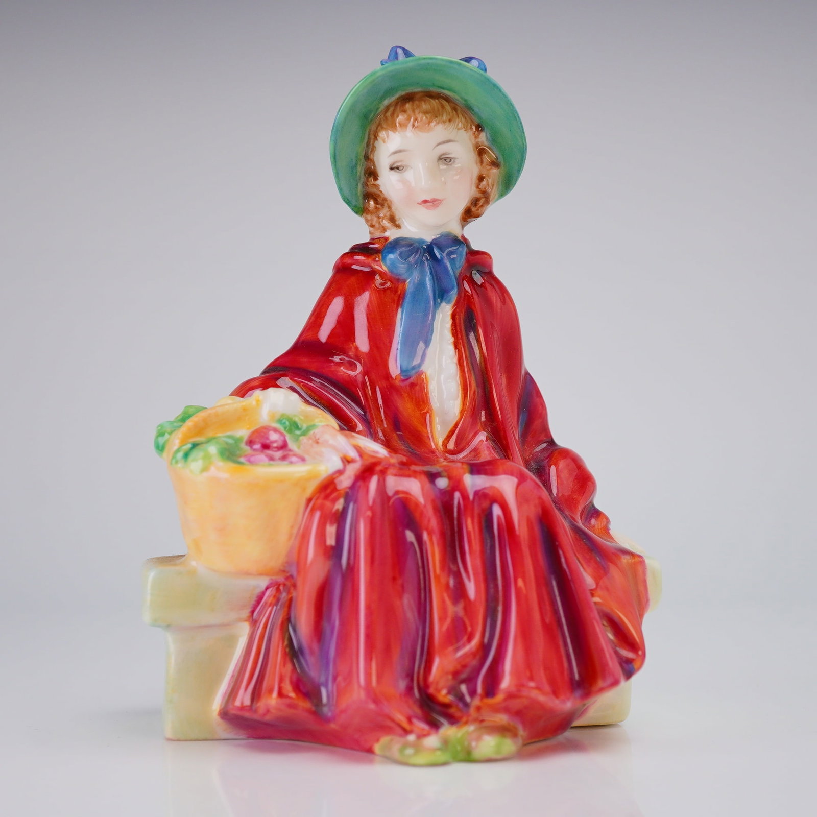 Royal Doulton Bone China Figurine Linda HN2106: A Royal Doulton Bone China Figurine, Linda (HN2106), depicting a woman in a red cape and green hat, marked COPR 1952. Dimensions: 3.25"L x 2.75"W x 4.75"H Weight: 8.10oz