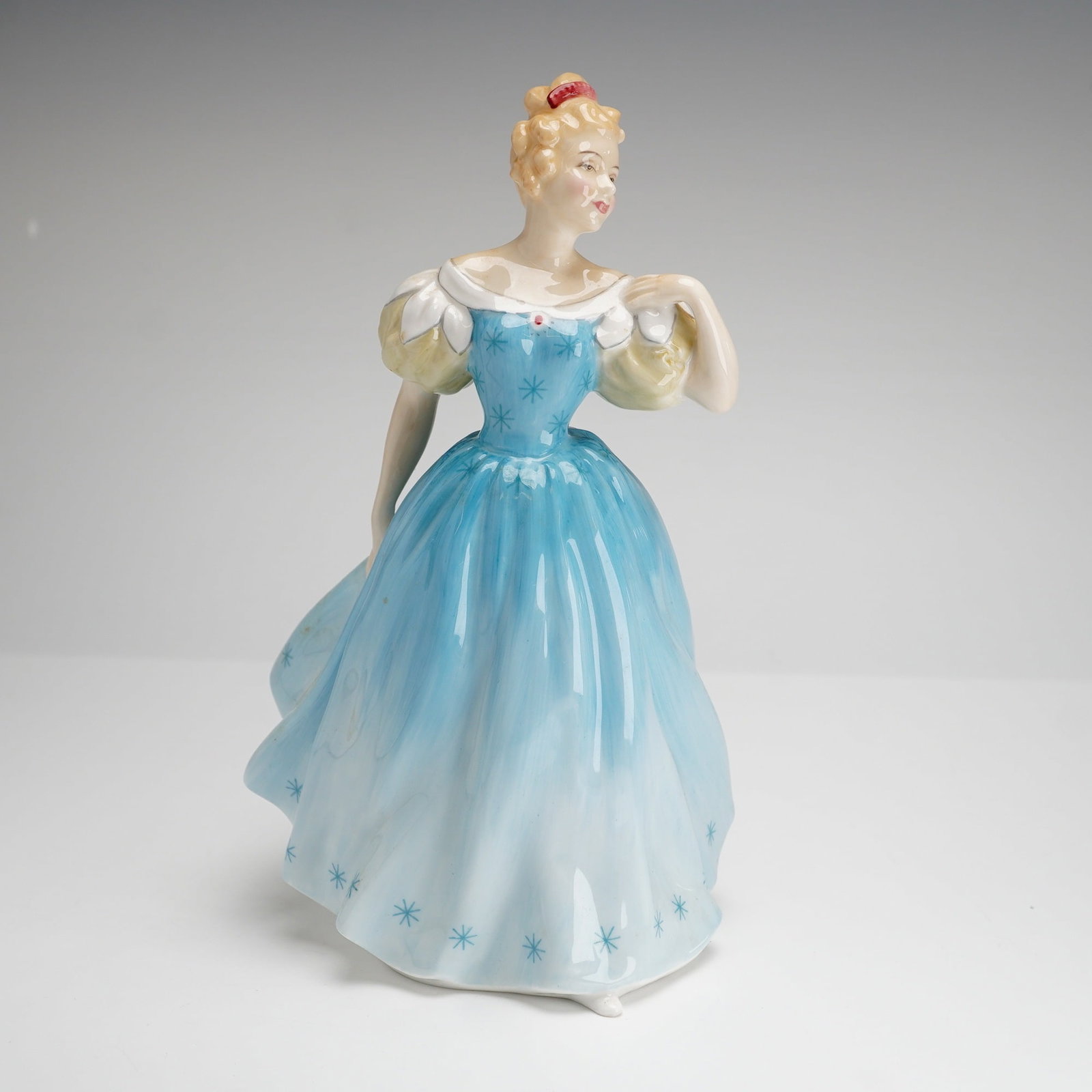 Royal Doulton Figurine, Enchantment HN 2178: This Royal Doulton figurine, titled Enchantment (model HN 2178), is a hand-painted bone china figure of a woman in a formal gown. This model features a garment with a gradient blue color accented by d