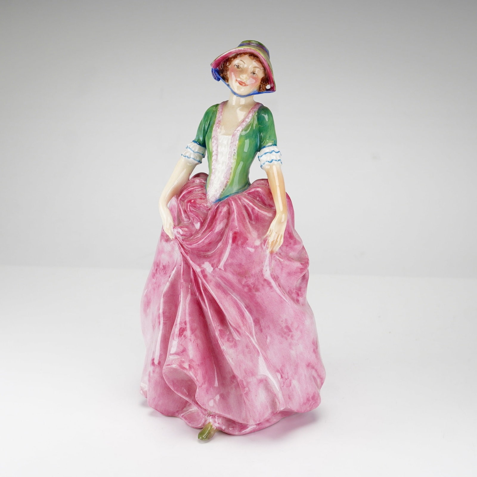 Royal Doulton Figurine, Vanessa HN1838: Hand painted and hand decorated figure of a beautifully smiling woman holding her pink dress, creating graceful wrinkles, and adorned with a green top complements the bottom color. Royal Doulton backs