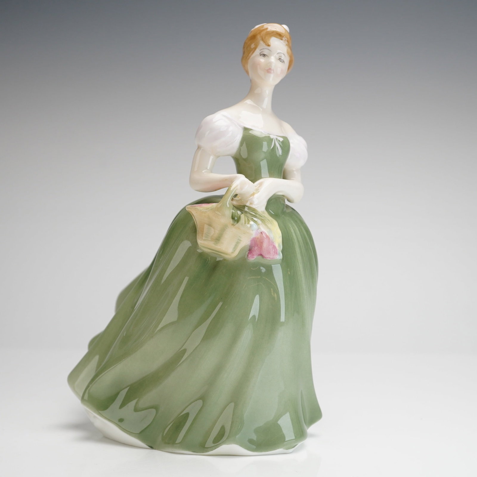 Royal Doulton Porcelain Figurine Clarissa HN 2345: The figure depicts a woman in a flowing green and white period gown with short puffed sleeves, holding a woven basket containing pink and yellow flowers, consistent with mid-20th-century decorative st