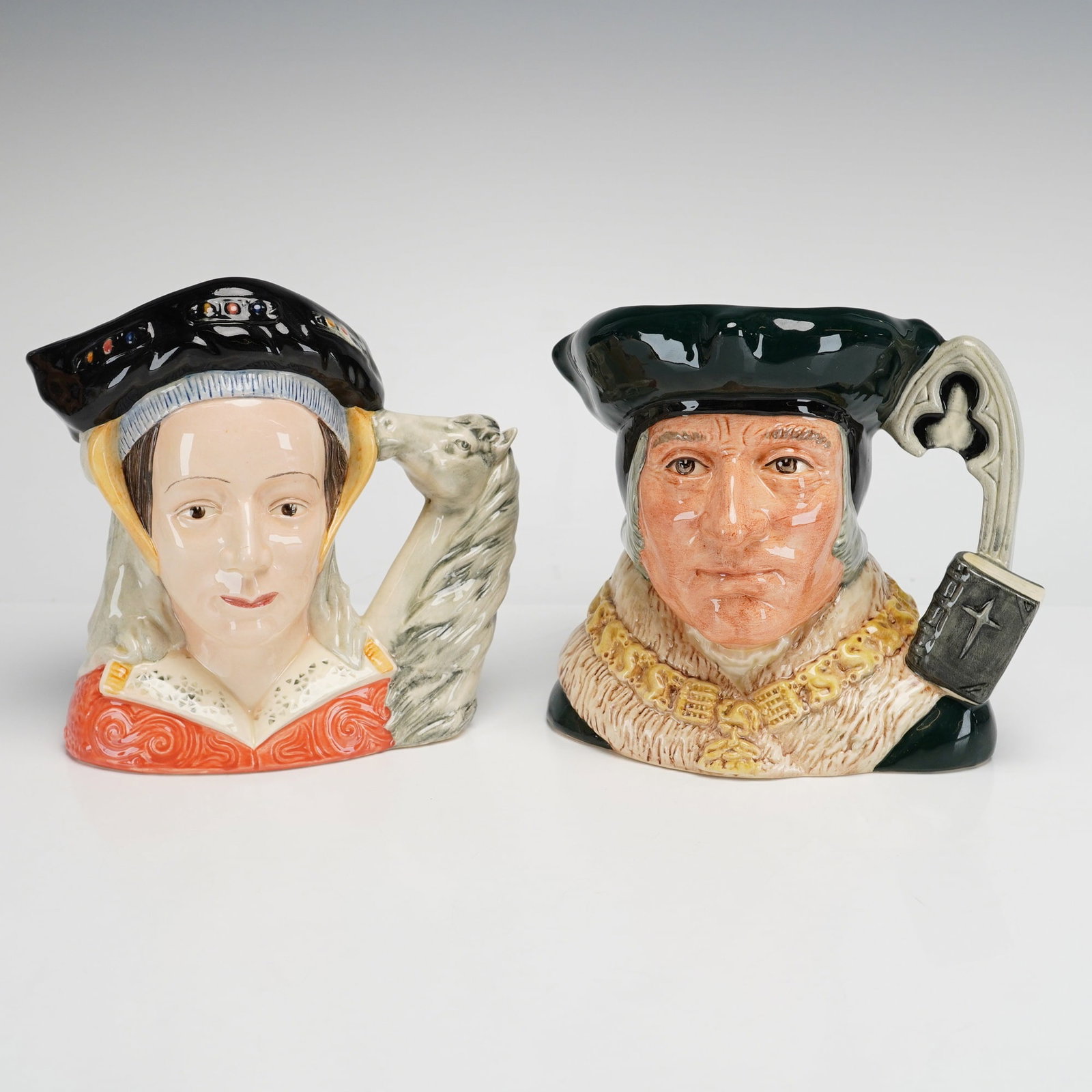 2pc Royal Doulton Large Character Jugs. Anne of Cleves D6653, Sir Thomas More D6792: This lot features two Royal Doulton hand-painted earthenware character jugs depicting notable historical figures from the Tudor era. The first jug depicts Anne of Cleves (model D6653), the fourth wife