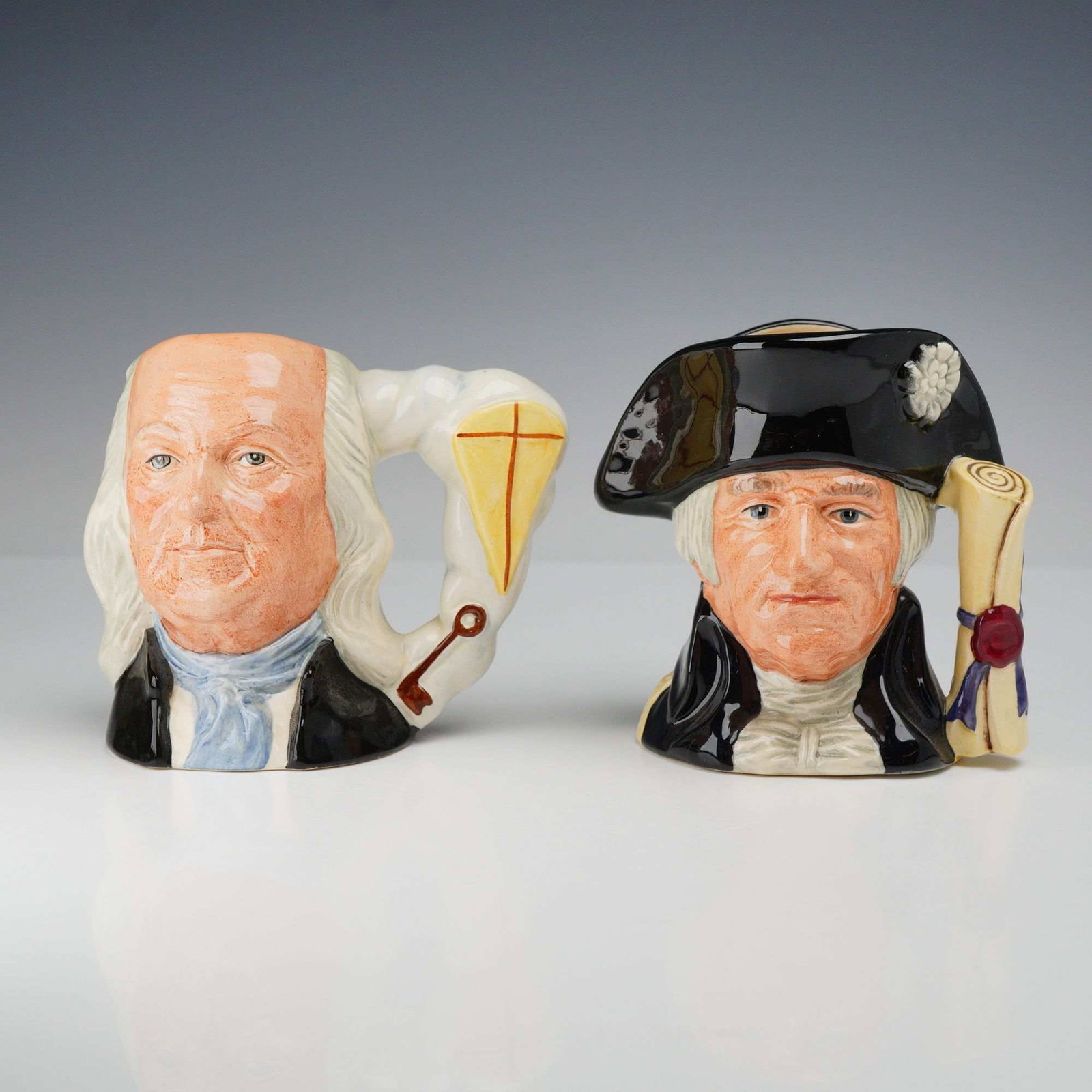 2pc Royal Doulton Small Character Jugs: A pair of small Royal Doulton earthenware character jugs featuring American historical figures Benjamin Franklin and George Washington. Each jug is hand decorated with realistic polychrome glazes. The