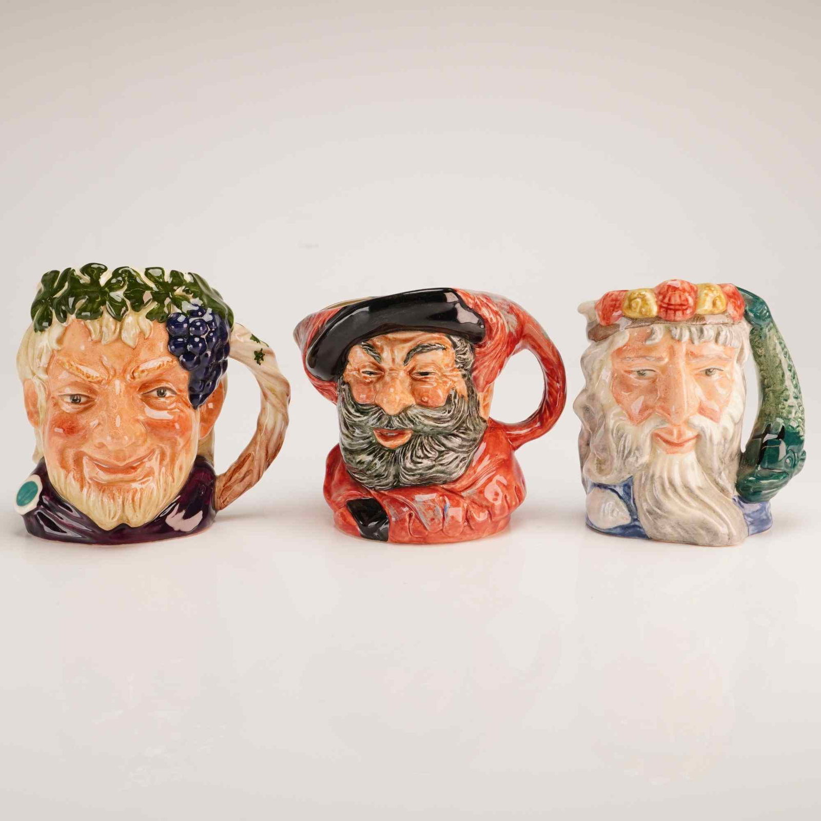 3pc Royal Doulton Small Character Jugs- D6505, 6385 and 6652: A trio of Royal Doulton glazed earthenware character jugs produced in England. Each jug is molded and finished with hand-painted underglaze decoration. The first jug depicts Bacchus, the Roman god of 