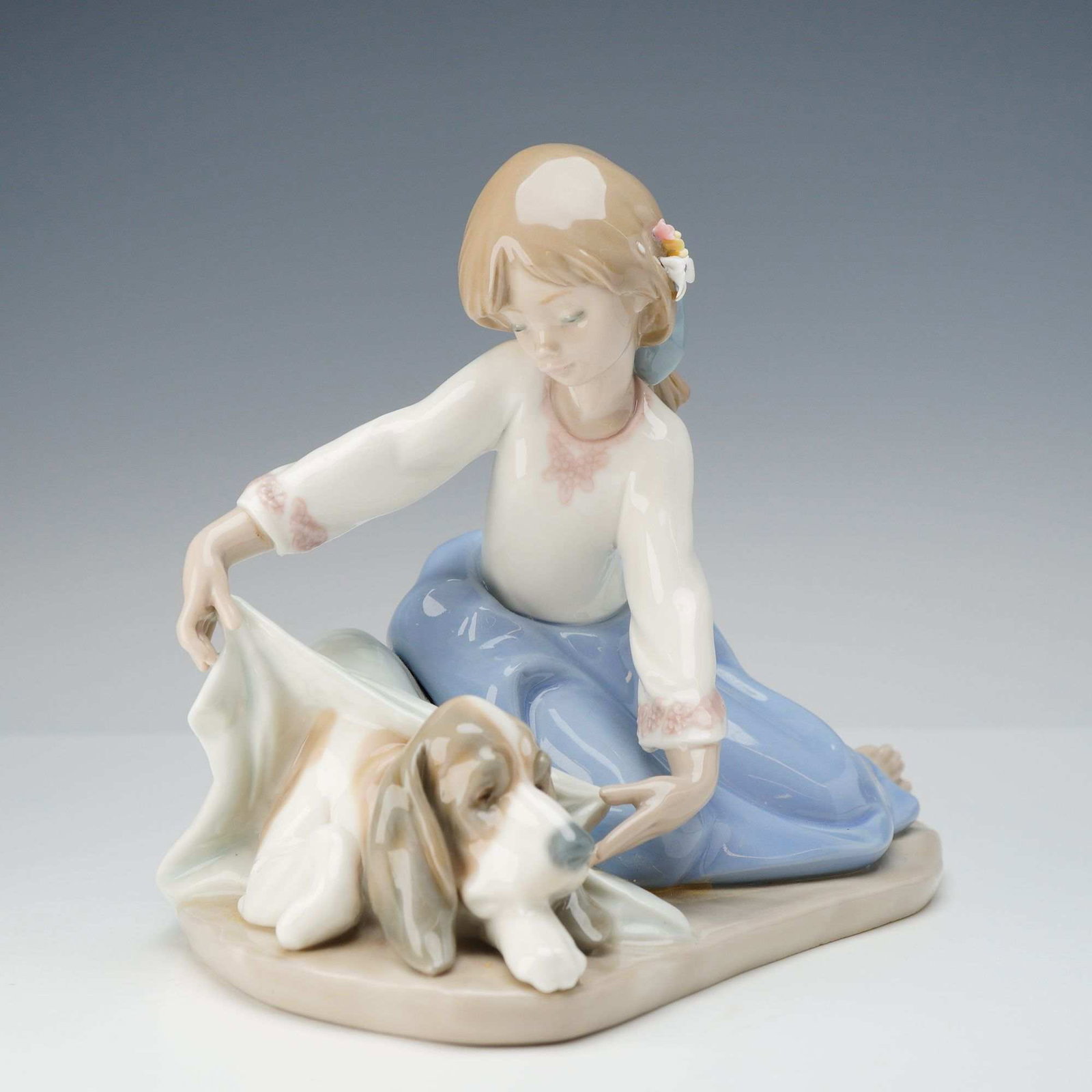 Lladro Porcelain Figurine, Dog's Best Friend 01005688: Designed by sculptor Antonio Ramos and first issued in 1990, this retired piece features a sentimental scene of a young girl tending to a sleeping basset hound. The girl is depicted in a seated pose w