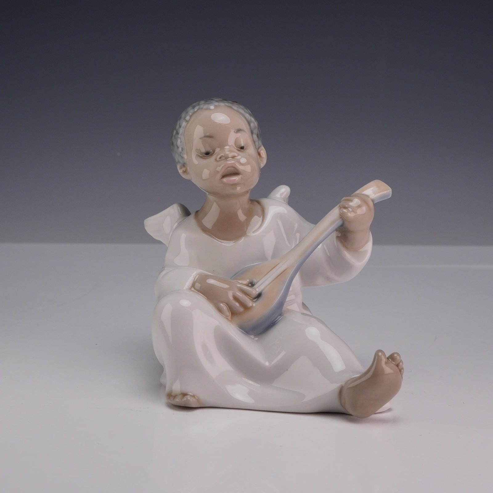 Lladro Porcelain Figurine Angel with Lute 01004537: Stamped Lladro porcelain figurine model number 4537, representing an angel playing a lute. This figurine, part of the Black Legacy collection, depicts a seated dark-skinned angel wearing a white robe 