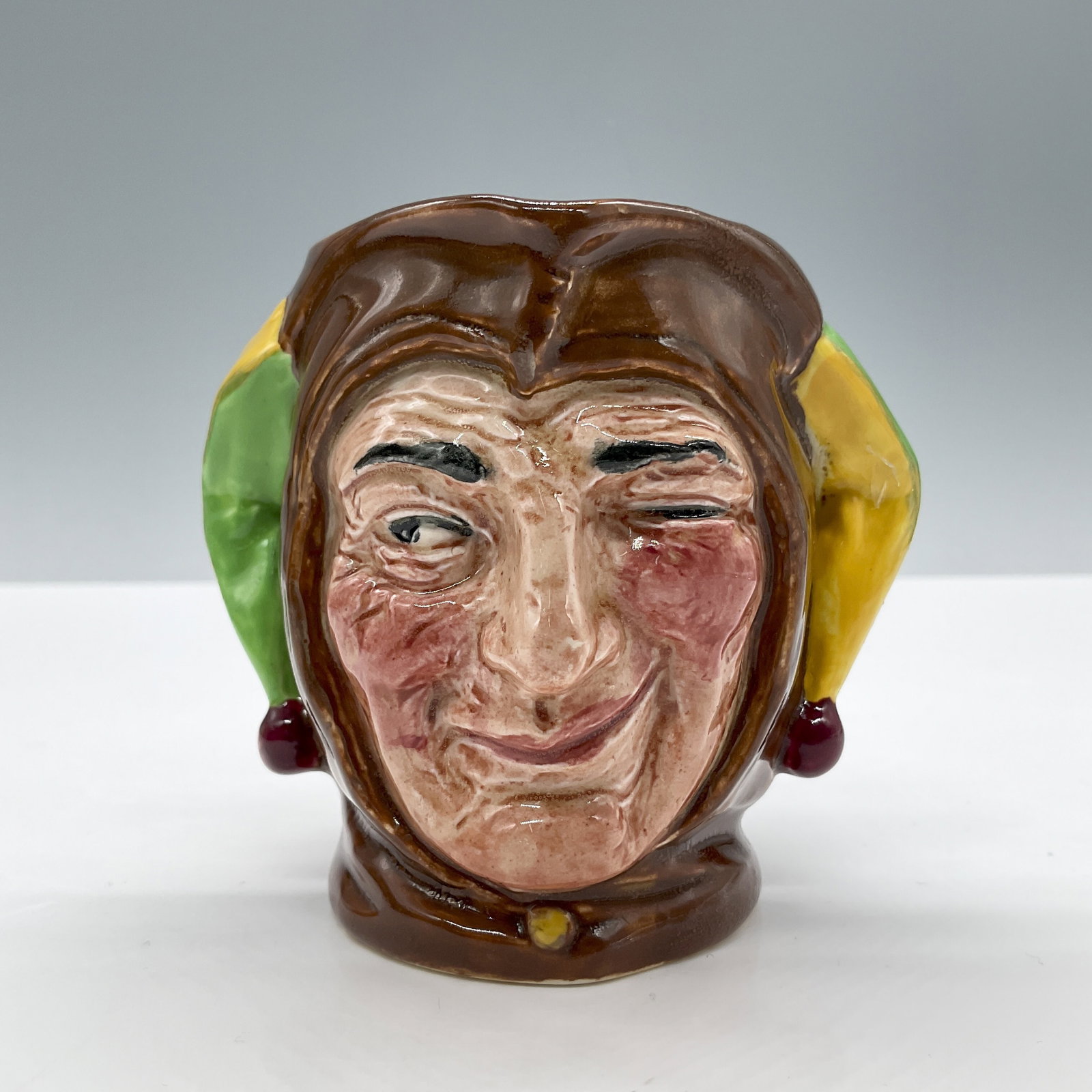 Jester D5556 - Small - Royal Doulton Character Jug: Brown, green and yellow coloration. Royal Doulton backstamp. Artist: Charles J. Noke Dimensions: 3.75"L x 3.5"W x 3.25"H Date or Era: 1936 - 1960 Manufacturer or Brand: Royal Doulton Country of Or