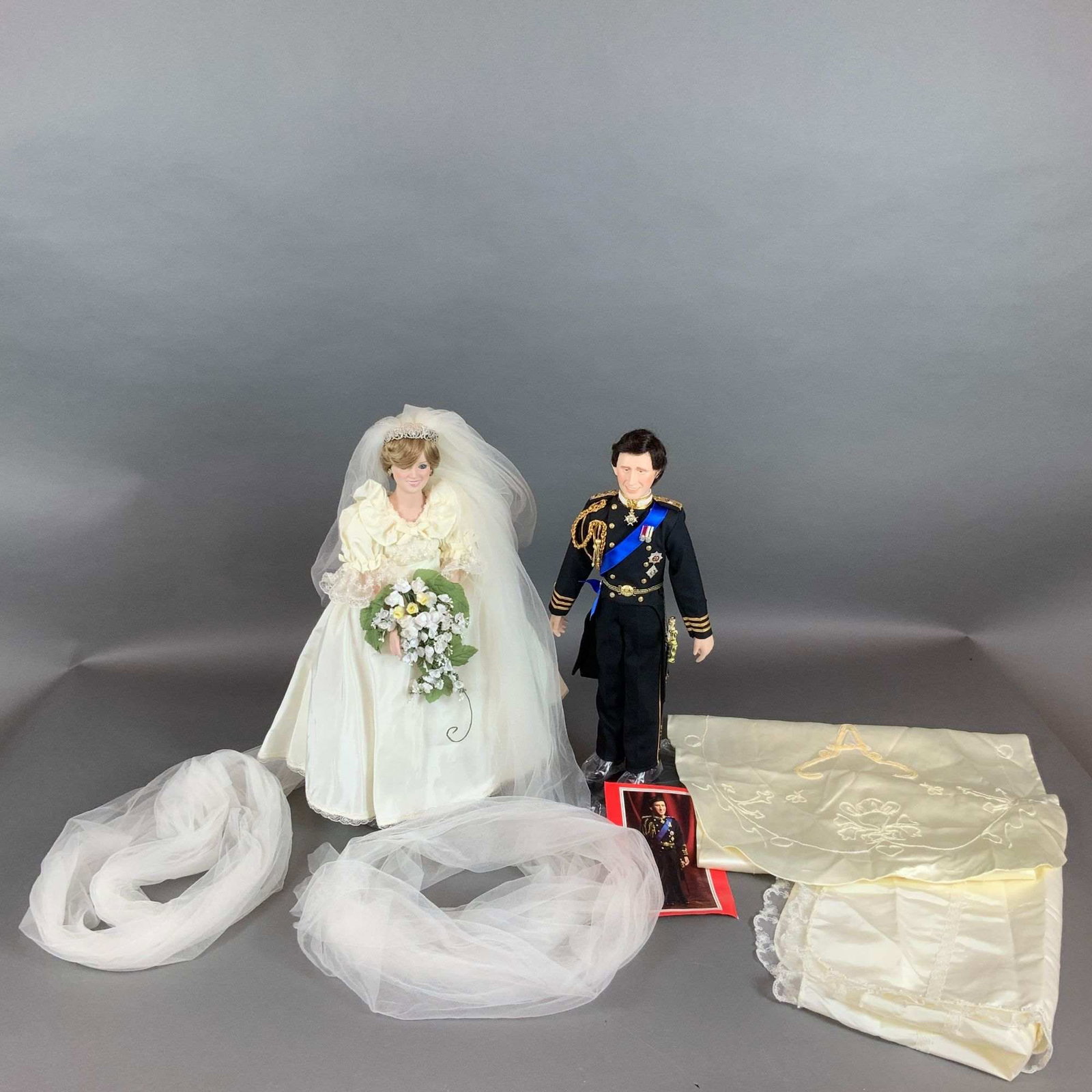 Two Danbury Mint Royal Wedding Dolls Depicting Prince Charles and Princess Diana with Stands: A set of two commemorative collector dolls by The Danbury Mint, depicting Prince Charles and Princess Diana in their attire from the Royal Wedding on July 29, 1981. These dolls are constructed with bi
