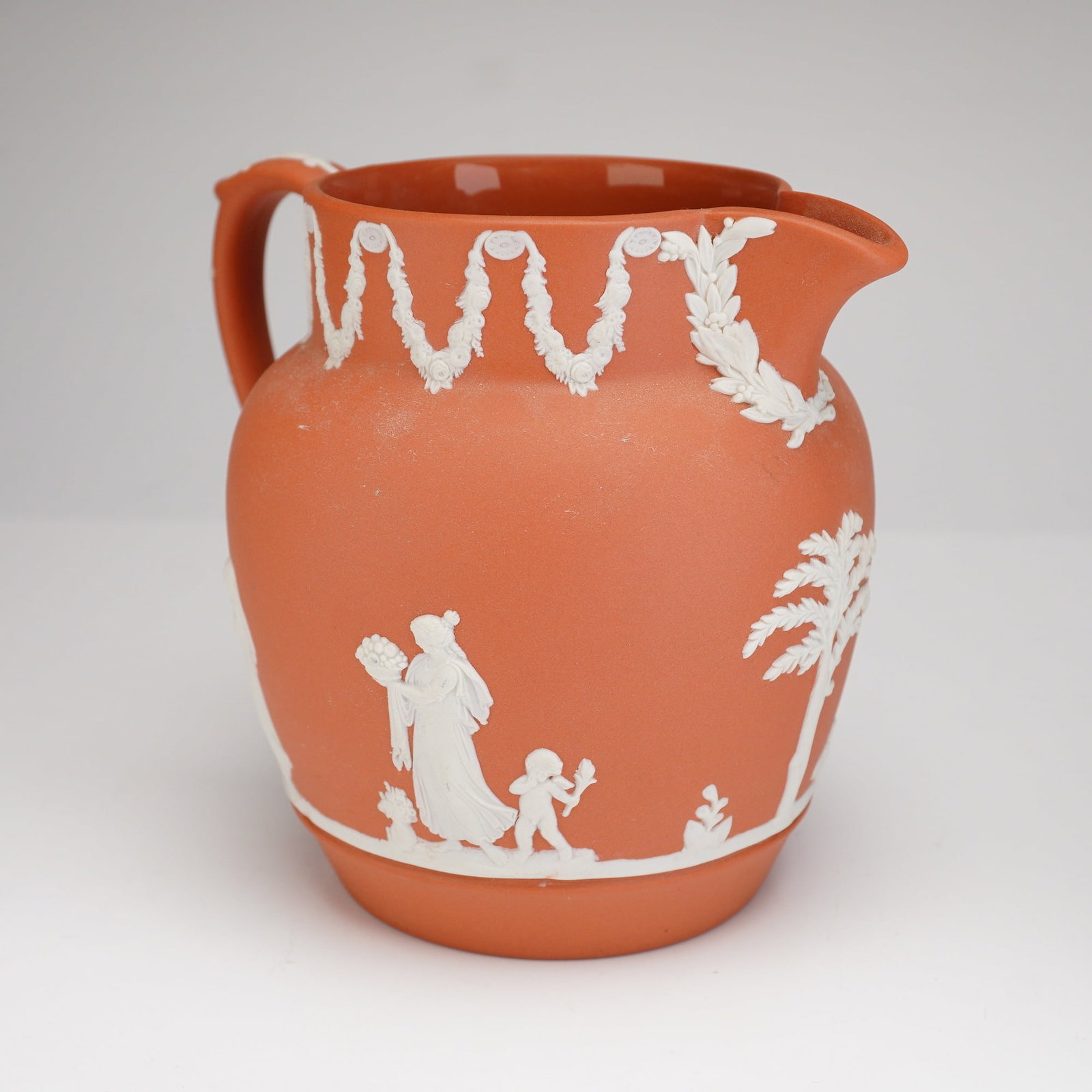 Wedgwood Terra Cotta Jasperware Pitcher: A Wedgwood terra cotta Jasperware pitcher crafted from fine-grained unglazed stoneware. The vessel features a bulbous body with a single loop handle and a pinched pouring spout. The exterior is finish