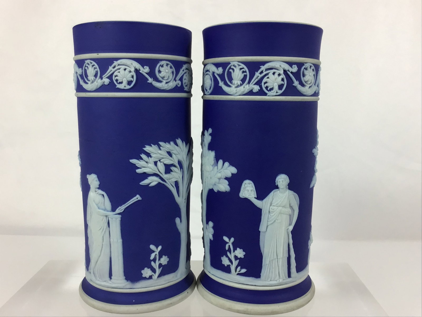 Pair of Wedgwood Cobalt Blue Jasperware Spill Vases: This set of 2 medium-large Wedgwood Jasperware cobalt blue spill vases is crafted from matte-finish stoneware. The cylindrical forms feature white bas-relief sprigging applied to a deep cobalt blue gr