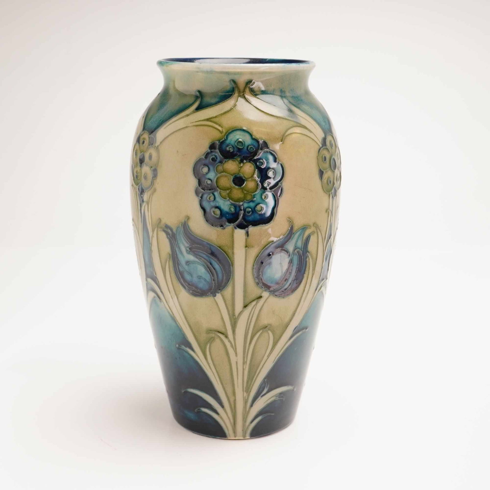 William Moorcroft Blue Floral Motif Vase: The vessel features an Art Nouveau decorative scheme of stylized floral motifs, including prominent tulips and circular flower heads. The decoration is executed using the tube-lining or slip-trailing 