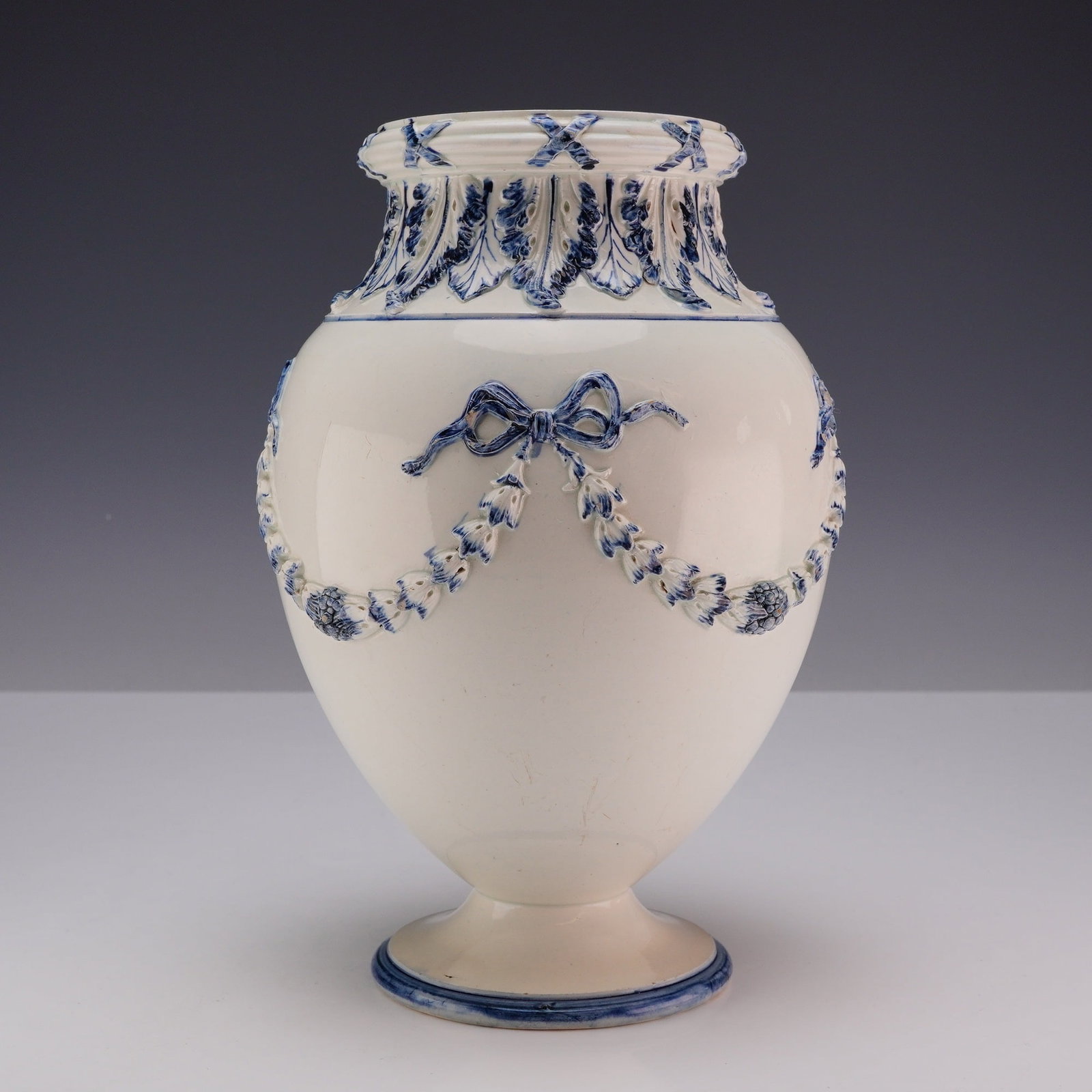 Wedgwood White and Blue Bow and Ribbon Design Ceramic Vase: A Wedgwood creamware ceramic vase of ovoid form featuring sprigged relief decoration in the neoclassical style. The body is ornamented with a pattern of floral garlands tied with ribbon bows, while th