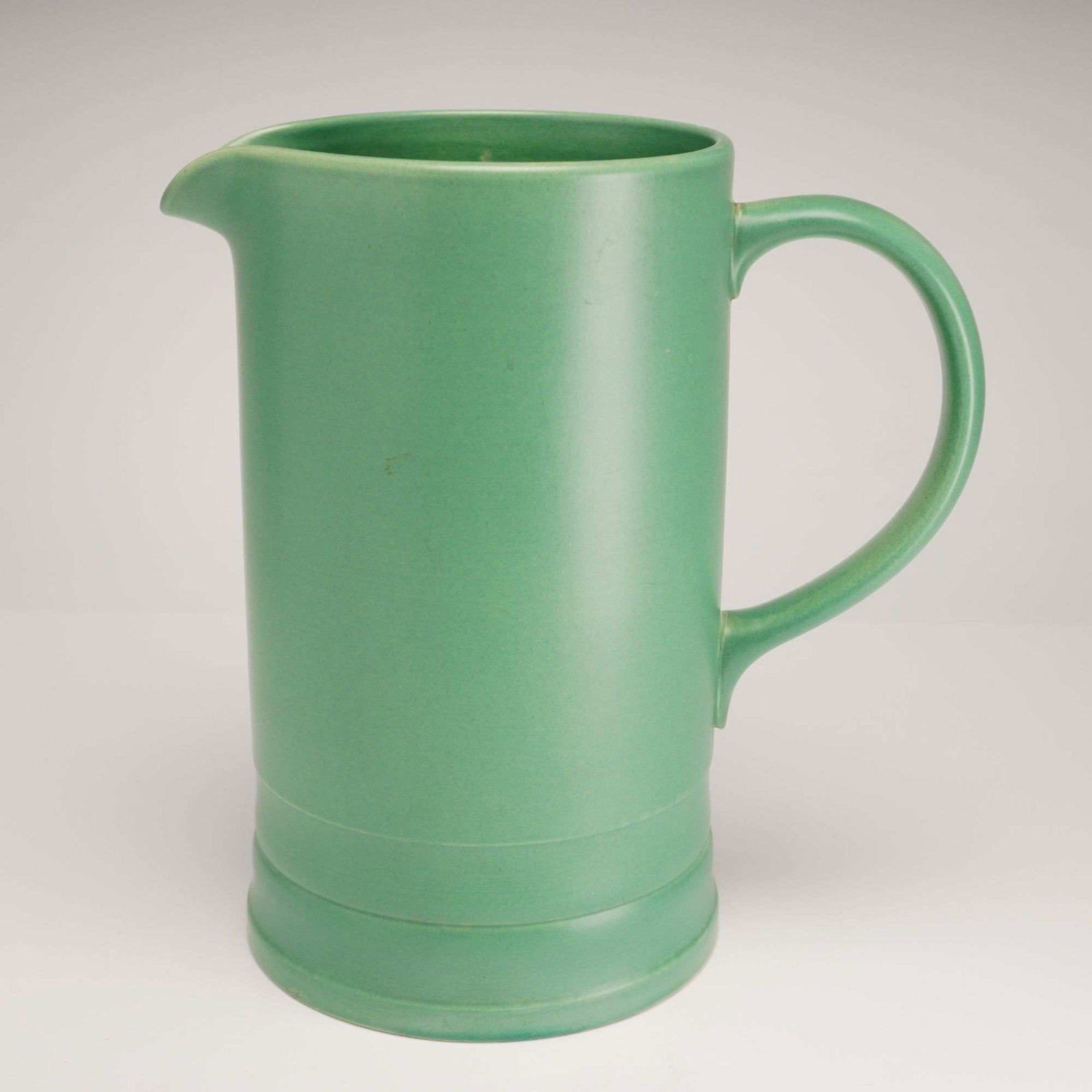 Keith Murray for Wedgwood Earthenware Pitcher: A Keith Murray for Wedgwood earthenware pitcher of cylindrical form, dating to the circa 1930s Art Deco period. The vessel is finished in a uniform monochrome Matt Green glaze, a signature color for M