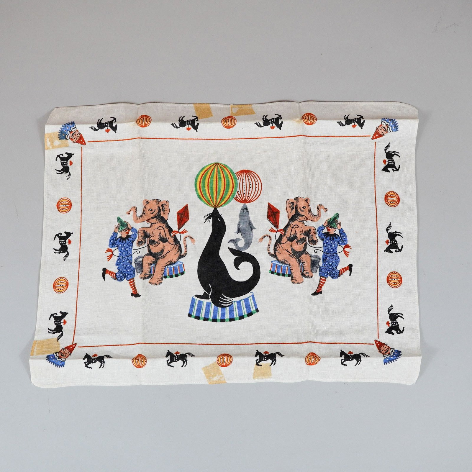 Vintage Mid-Century Modern Circus Theme Screen Printed Tea Towel: A rectangular tea towel crafted from a natural fiber, likely linen or a linen-cotton blend. The piece features a whimsical, mid-century modern circus motif executed in screen print. The central design