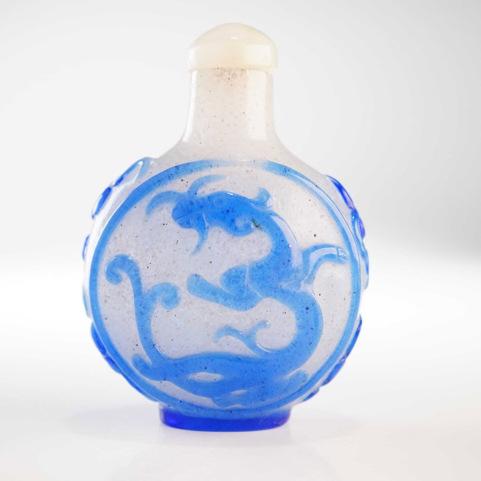 Peking Glass Snuff Bottle, Blue Overlay Chilongs: Adorned with a blue relief overlay, this clear snowflake-patterned Peking glass snuff bottle features chilongs and double gourd shapes. It is topped with a clear quartz-toned stopper. Dimensions: 1.5"
