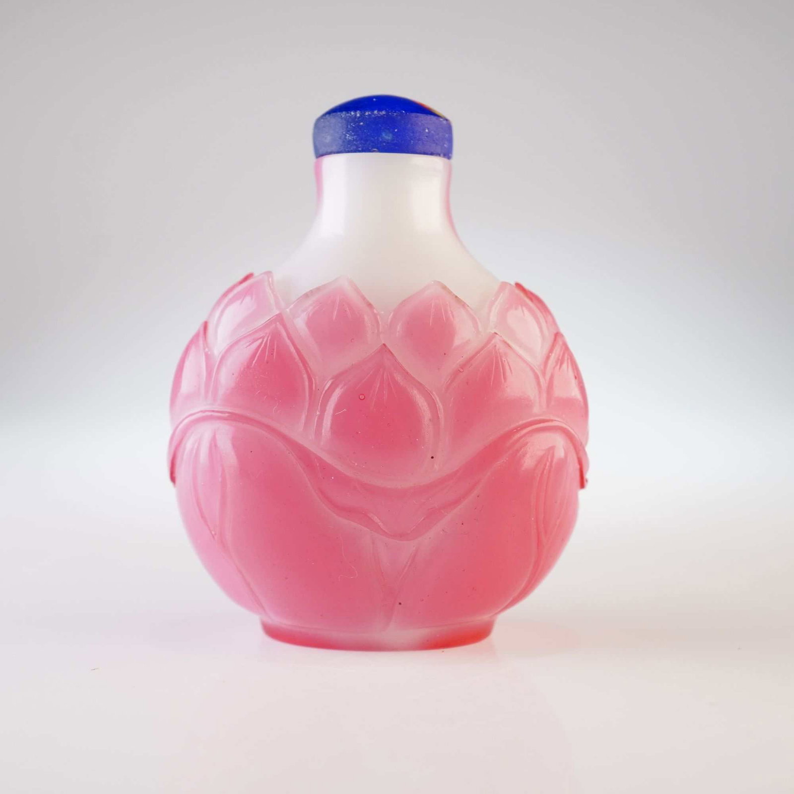 Peking Glass Snuff Bottle, Pink Overlay Lotus Design: Decorated with a pink overlay in a lotus flower pattern, this round white Peking glass snuff bottle is topped with a blue stopper accented with red and yellow. Dimensions: 1.75"L x 1.25"W x 2.25"H Wei