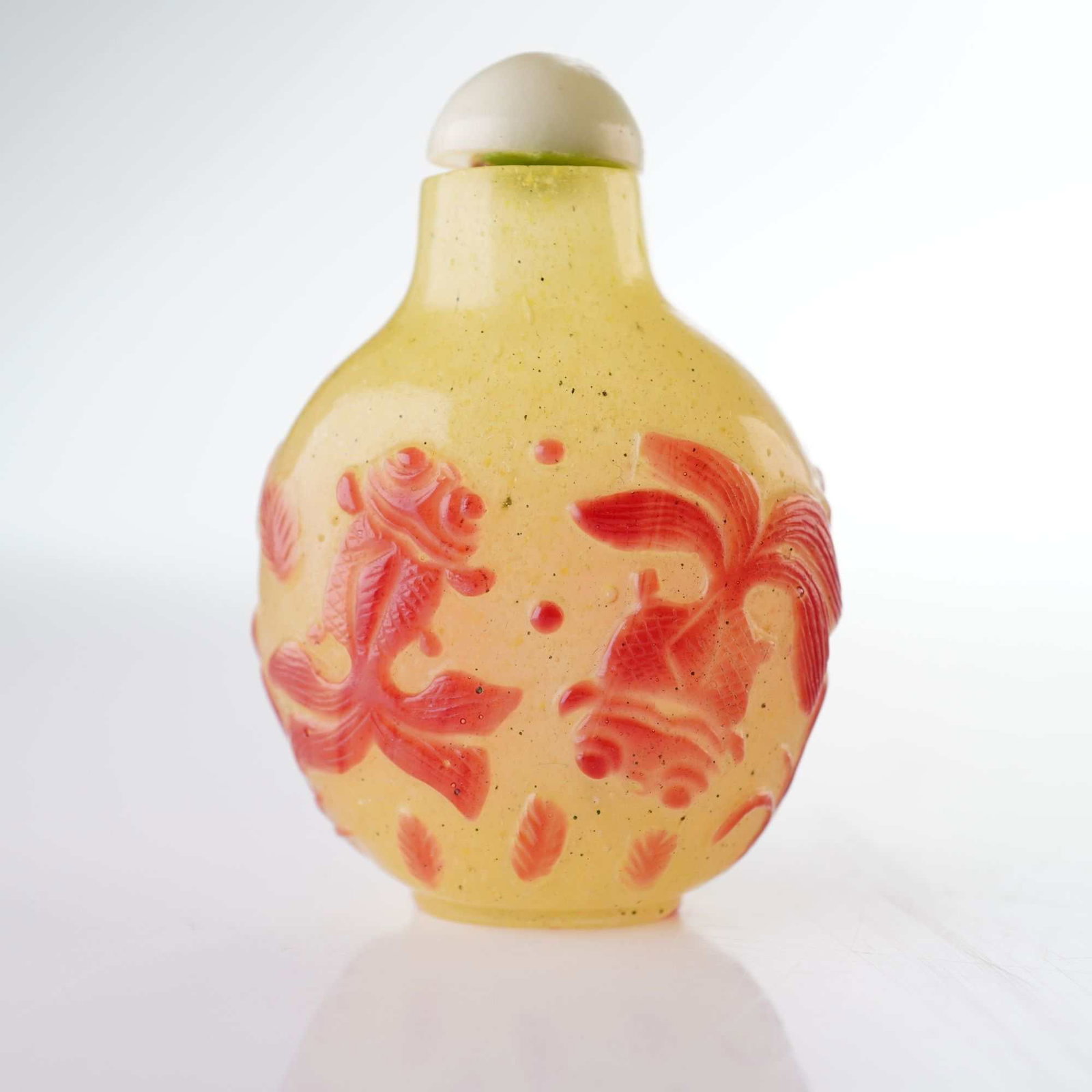 Peking Glass Snuff Bottle, Yellow with Red Fish Overlay: A yellow round snuff bottle adorned with red-hued high relief figures depicting fish swimming underwater. It is topped with a milky light green stopper. Dimensions: 1.5"L x 1"W x 2.25"H Weight: 1.5 oz