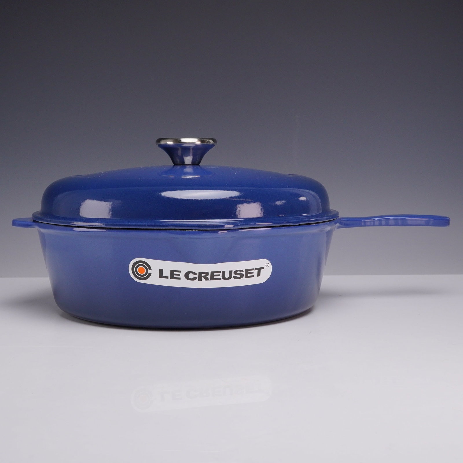 Le Creuset Cobalt Blue Enameled Cast Iron Round Skillet with Lid: A contemporary Le Creuset enameled cast iron deep round skillet finished in cobalt blue with a matching domed lid. The pan construction includes a long primary handle, a tab-style helper handle, and d