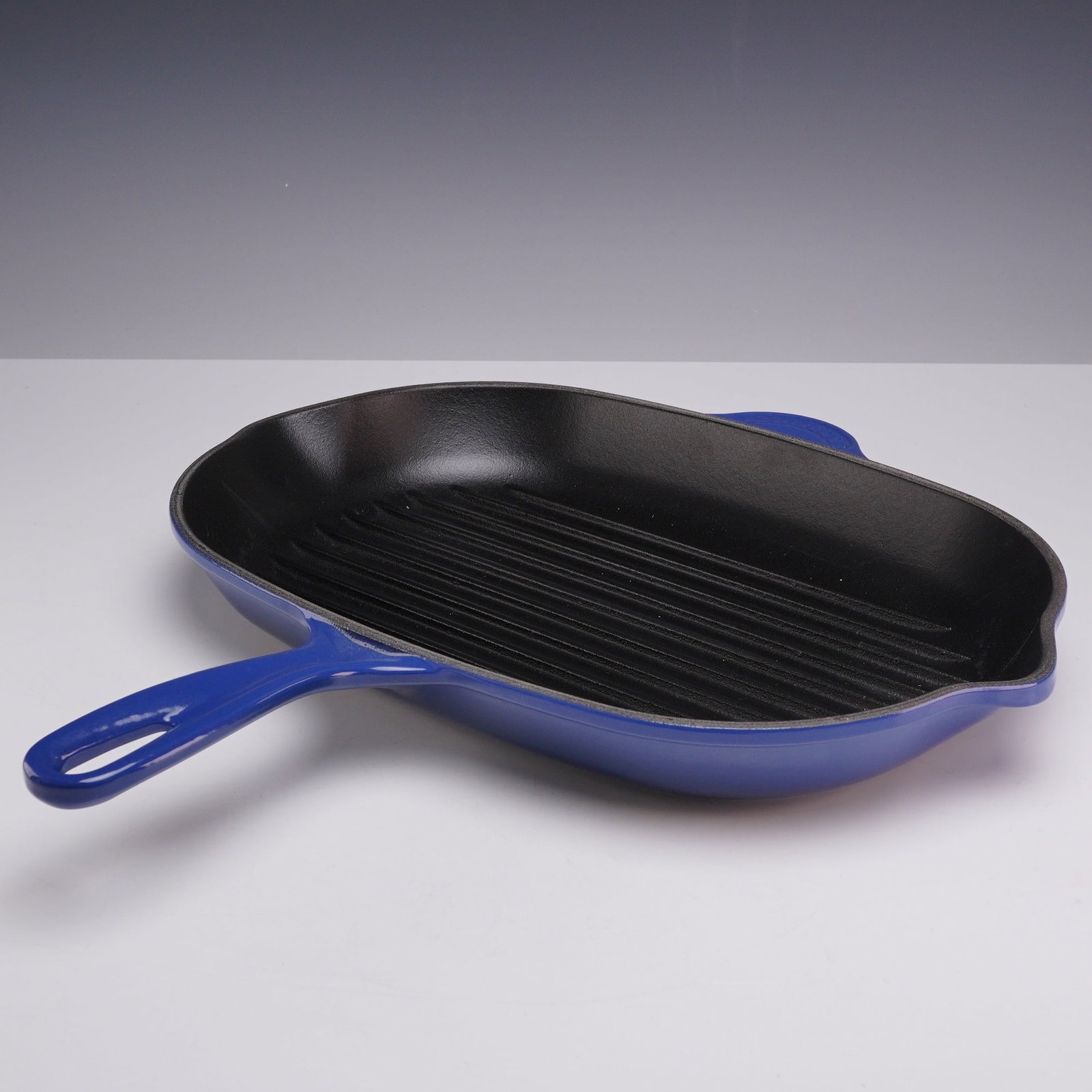 Le Creuset Cobalt Enameled Cast Iron Grillit Skillet Grill Pan: A Le Creuset enameled cast iron grillit skillet grill pan finished in cobalt blue. The pan features a matte black enameled interior with a ridged cooking surface. It is designed with two integrated po