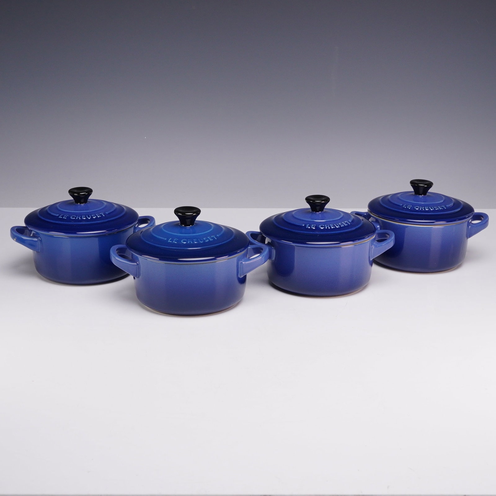 Set of Four Le Creuset Cobalt Enameled Cast Iron Petite Casserole Baking Dishes with Lids: This lot consists of a set of four Le Creuset cobalt enameled cast iron petite casserole baking dishes, each accompanied by a matching lid. These round miniature vessels, also known as mini cocottes, 