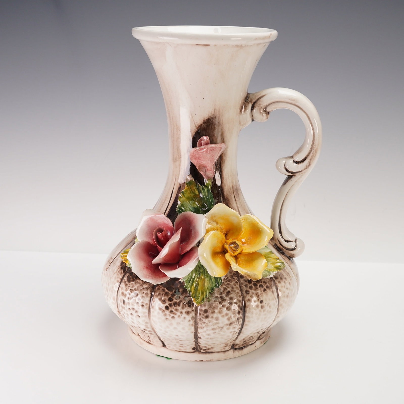 Capodimonte Vintage Floral Porcelain Pitcher: Elegant hand-painted Italian porcelain vase featuring a curvaceous, fluted neck with a scrolled handle and a textured bulbous body in soft beige tones. Adorned with delicate applied porcelain flowers