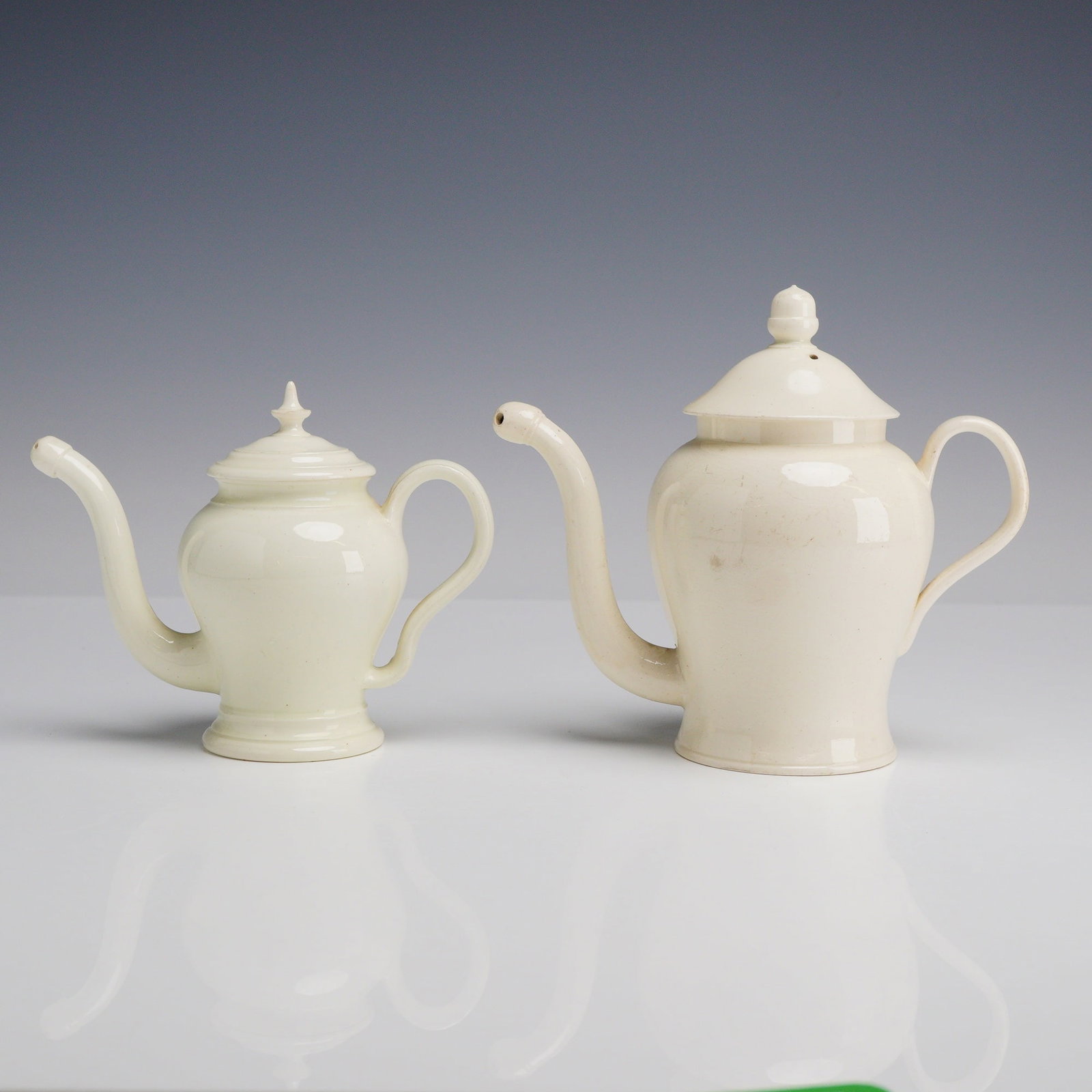 2pc Creamware Bubby Pots: This group of ceramic bubby pots consists of two lidded pots crafted in the style of late 18th or early 19th-century creamware. The pieces are composed of cream-colored lead-glazed earthenware with a