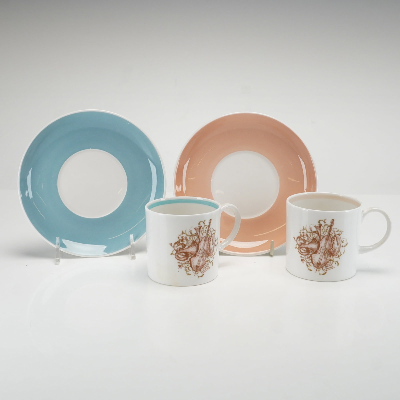 4pc Susie Cooper Bone China Musical Coffee Cups and Saucers: This pair of bone china coffee cups and matching saucers was designed by Susie Cooper and features the Musical Instruments pattern. Each cup is decorated with a central brown transfer-printed motif