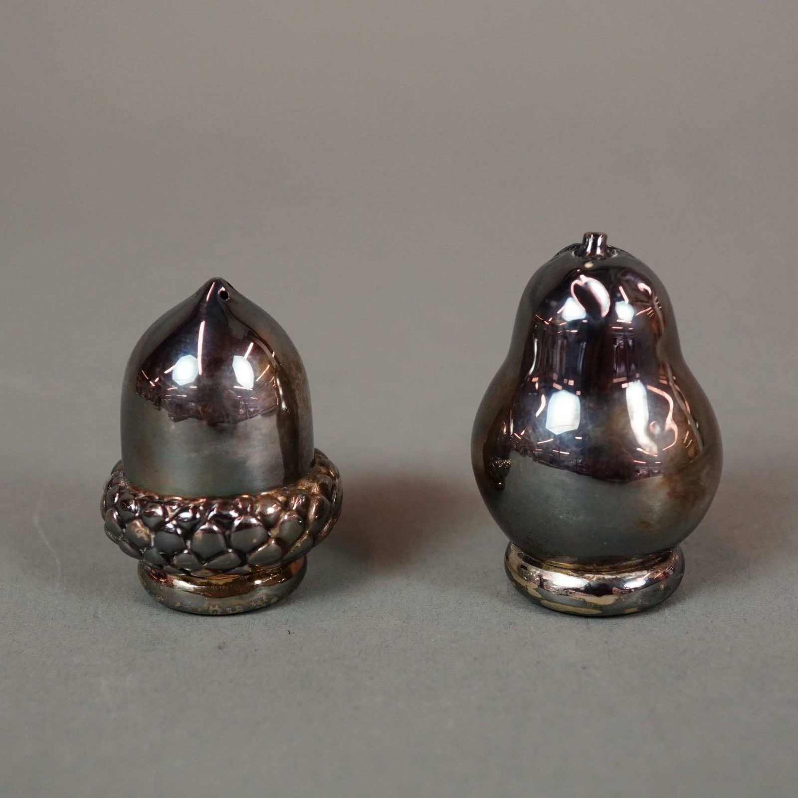 Pair of Tiffany & Co. Sterling Silver Acorn and Pear Salt and Pepper Shakers: A two-piece set of sterling silver novelty salt and pepper shakers manufactured by Tiffany & Co. The set comprises two naturalistic forms: one shaker is modeled as an acorn with a smooth body and a