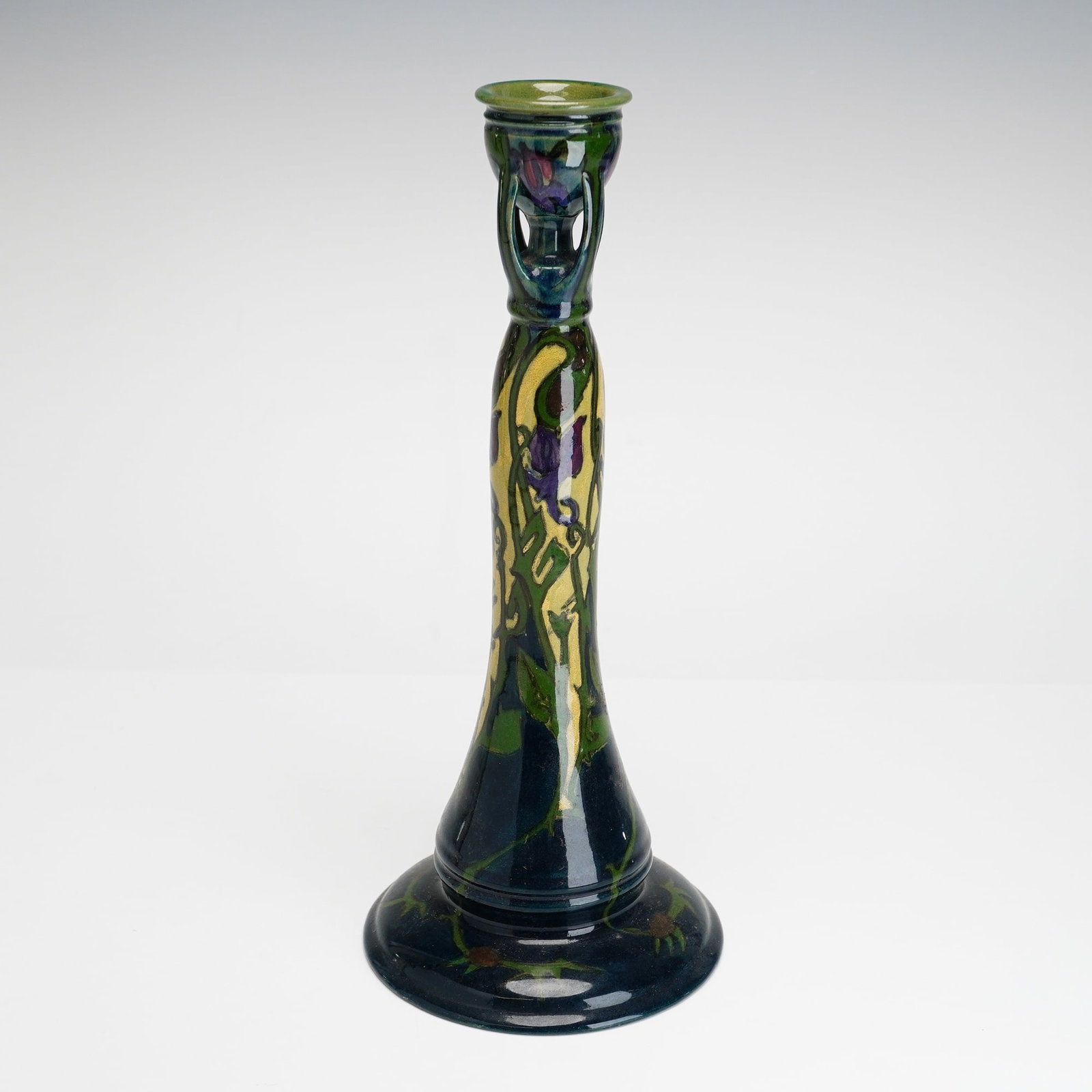 Gouda Art Nouveau Floral Pottery Candlestick: A tall Dutch Art Nouveau earthenware candlestick produced by a Gouda pottery manufactory. The vessel features a wide, flared circular base that tapers into a long, slender column and concludes in a cu