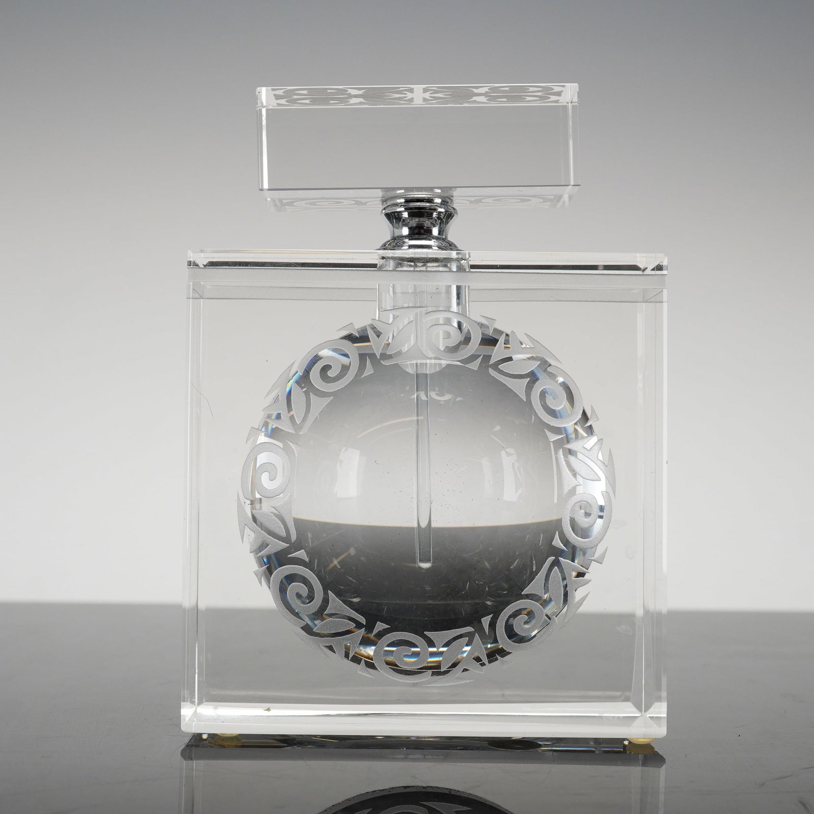 Scrollwork Relief Art Contemporary Crystal Perfume Bottle: A contemporary clear crystal perfume bottle. The piece is designed as a solid, polished rectangular block with a spherical interior reservoir. The reservoir features an etched circular band of frosted