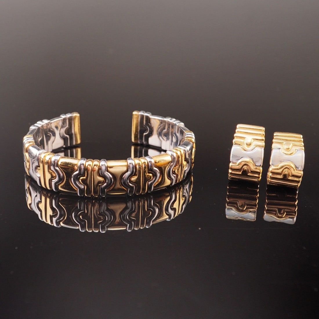 18K Yellow Gold and Steel Parentesi Style Cuff Bracelet and Earrings: A three piece set comprising a bangle and a pair of earrings, each featuring a curved geometric design. The earrings have clip-back closures. Each item is marked 750, with the bangle additionally mark
